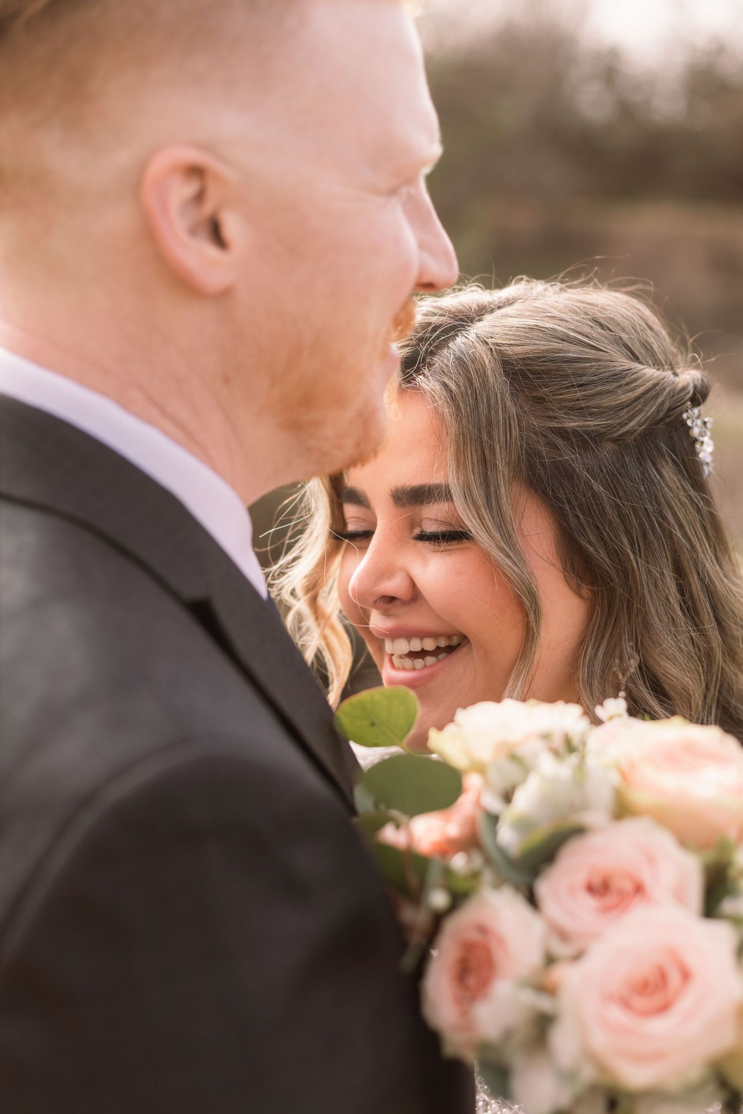 A romantic wedding moment captured with blush pink roses in the foreground during a sunny outdoor celebration.