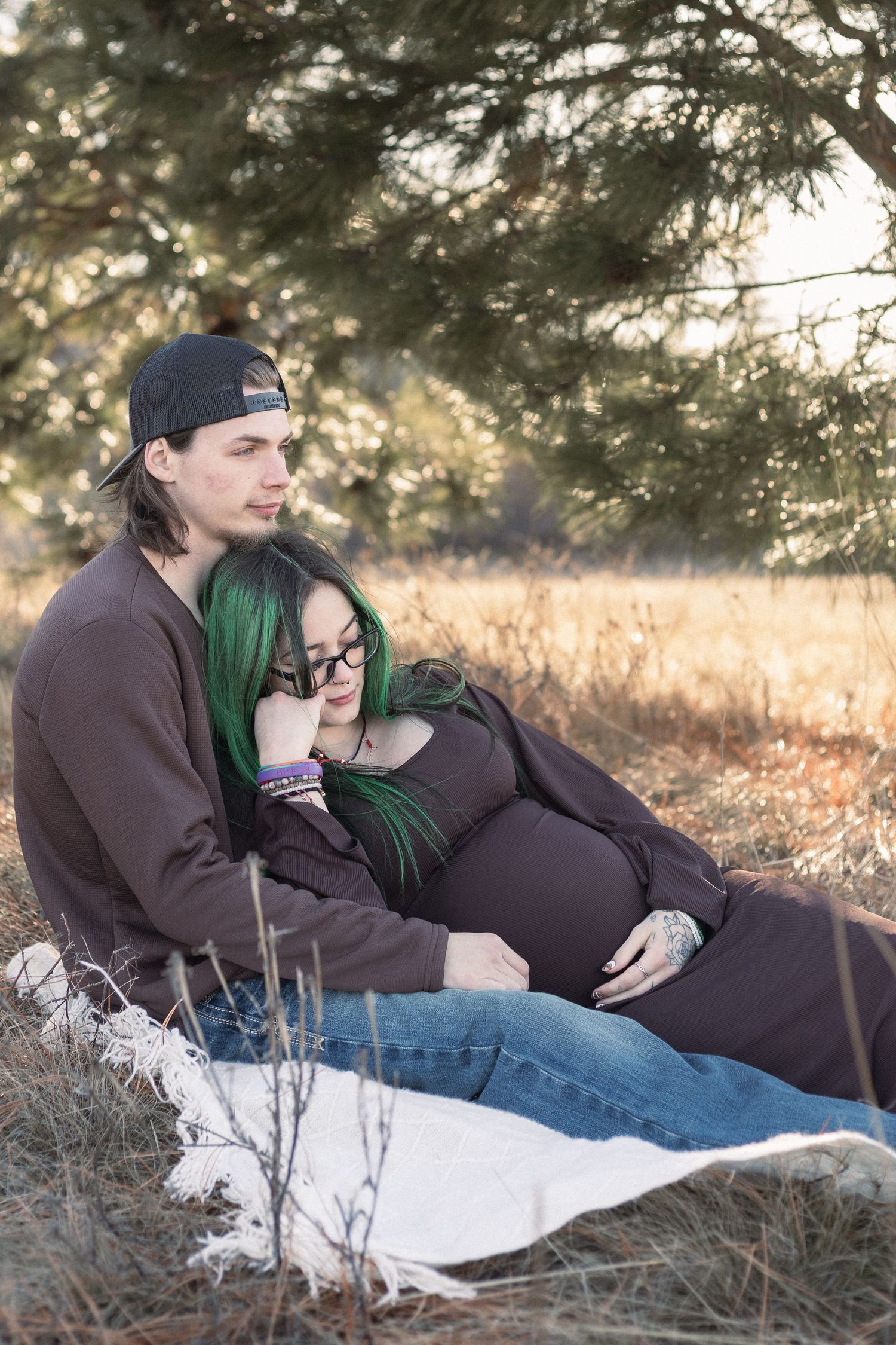 Couple sharing intimate moment during outdoor maternity photoshoot on blanket.