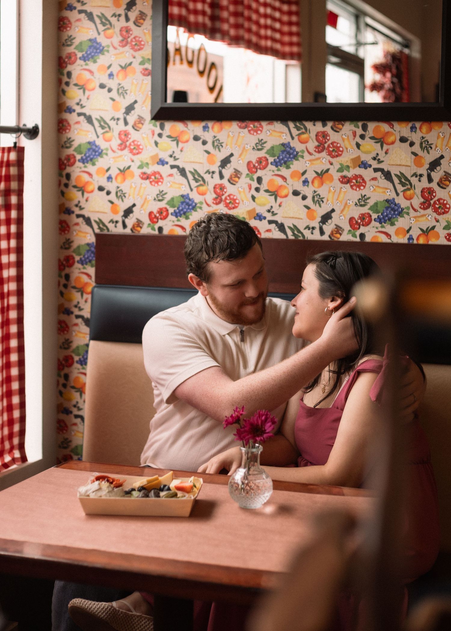 A couple shares a romantic moment in a restaurant booth with red checkered curtains.
