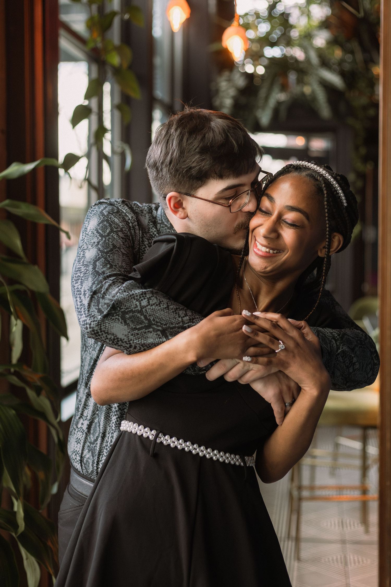 A romantic couple embraces and shares a tender moment together in a warmly lit indoor setting with plants.