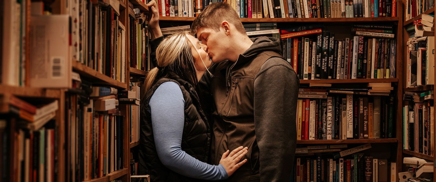 A romantic moment between two people sharing an intimate embrace in a cozy library surrounded by bookshelves.