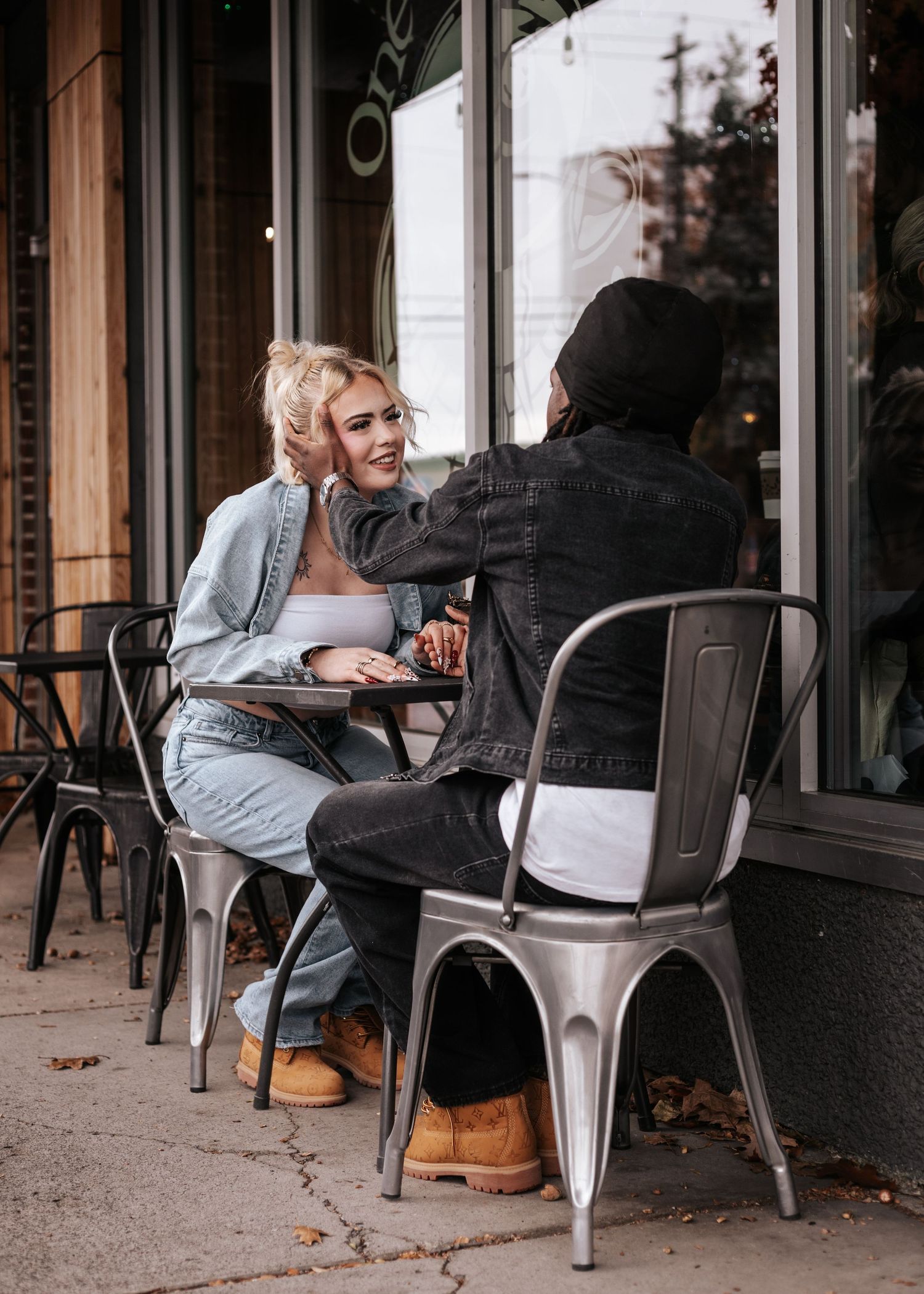 Two people having coffee and conversation at an outdoor cafe with metal chairs on a city sidewalk.