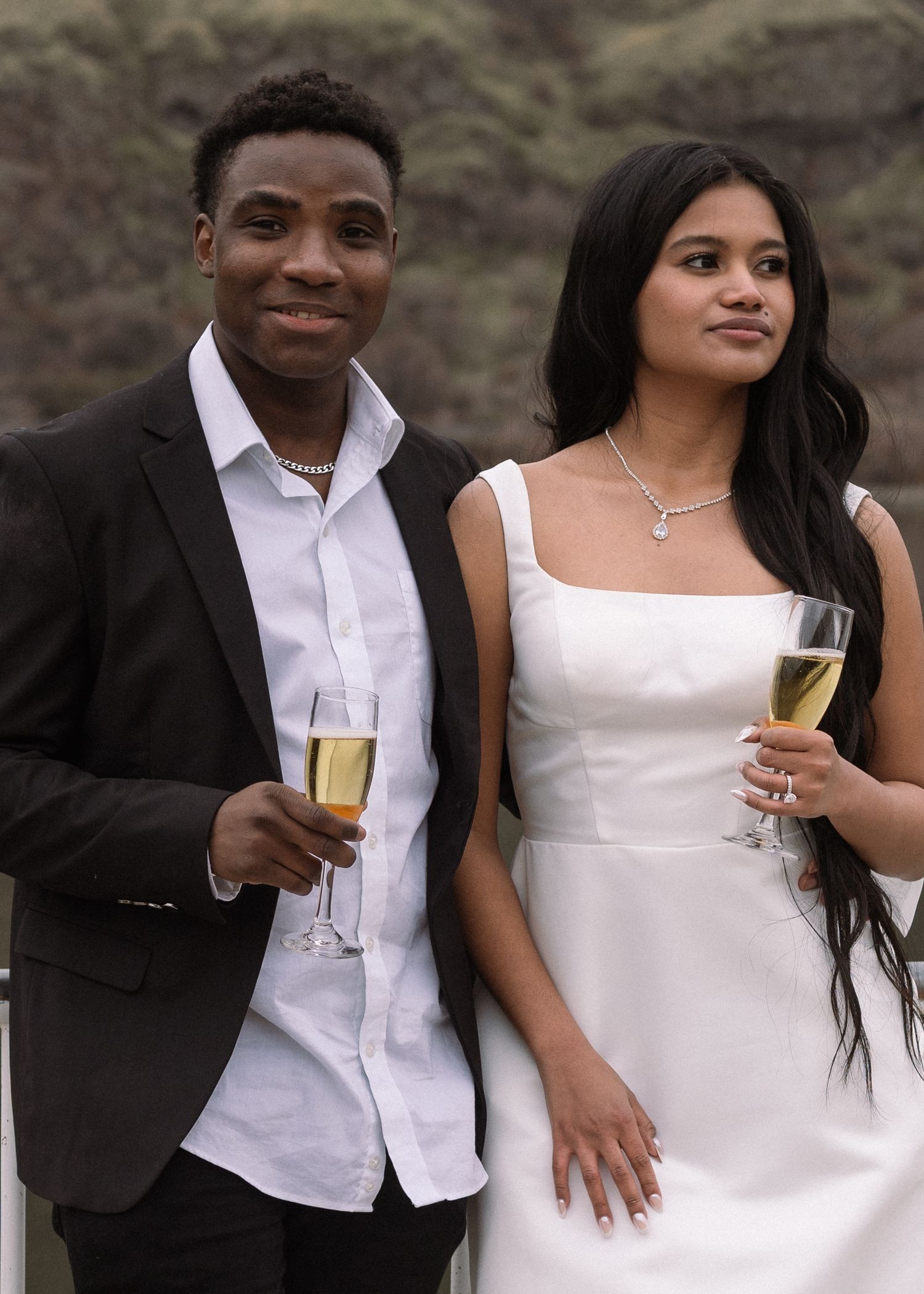 A couple in formal attire holding champagne glasses at an outdoor celebration.