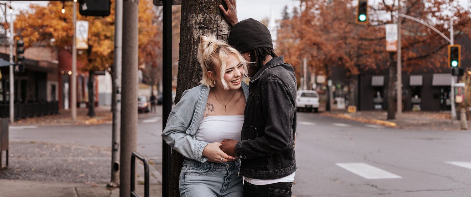 Two people share a warm embrace on an autumn street lined with orange-leaved trees.