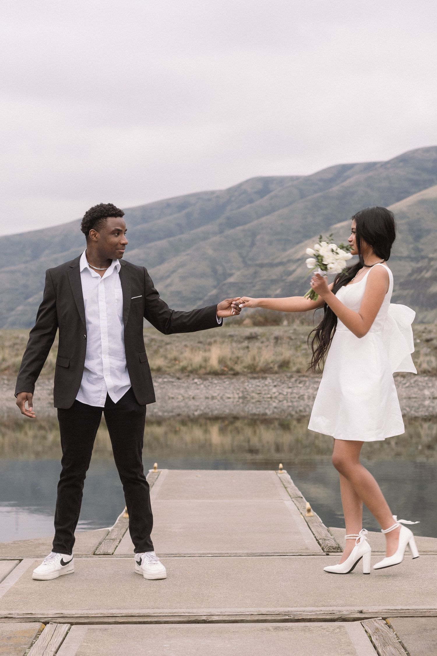 A couple dancing playfully on a dock by a mountain lake.
