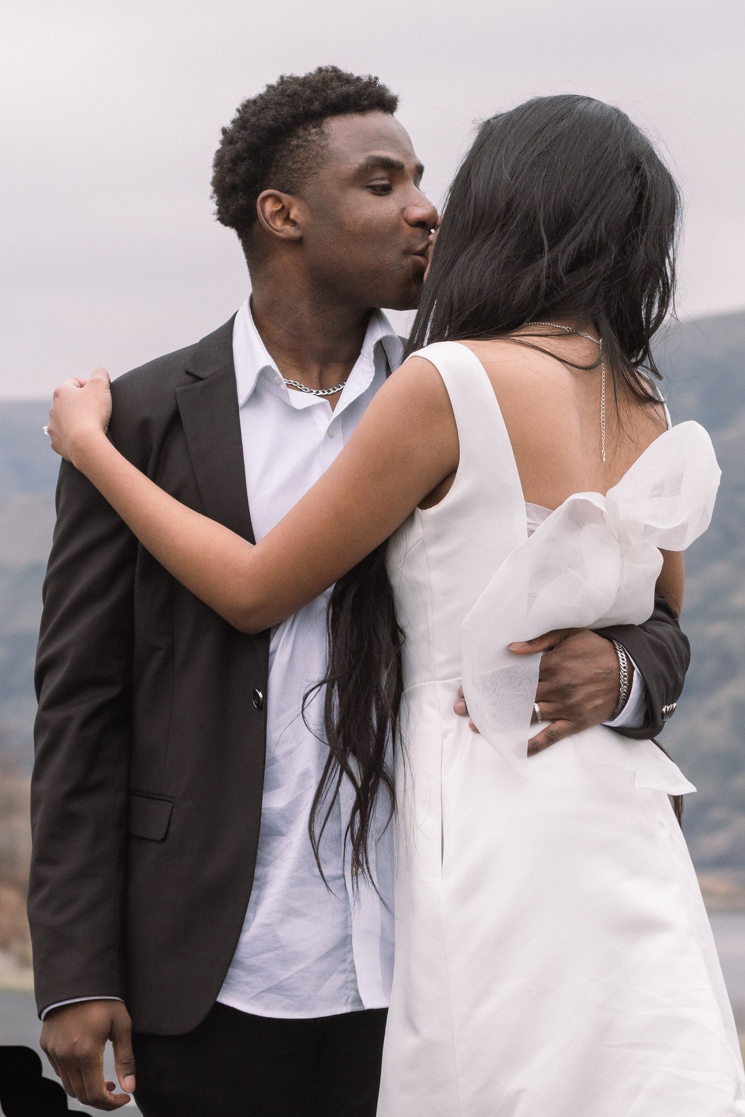 A romantic embrace between a couple in formal wedding attire against a mountain backdrop.