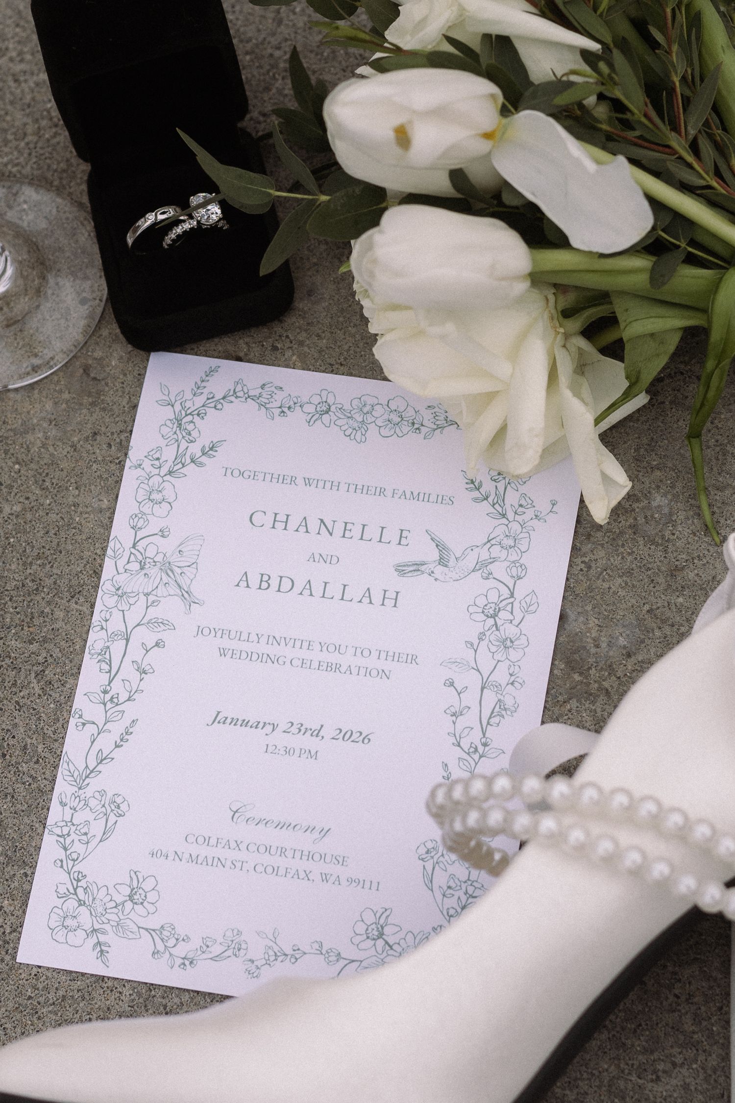 Wedding invitation with pearl necklace and white flowers on gray surface.