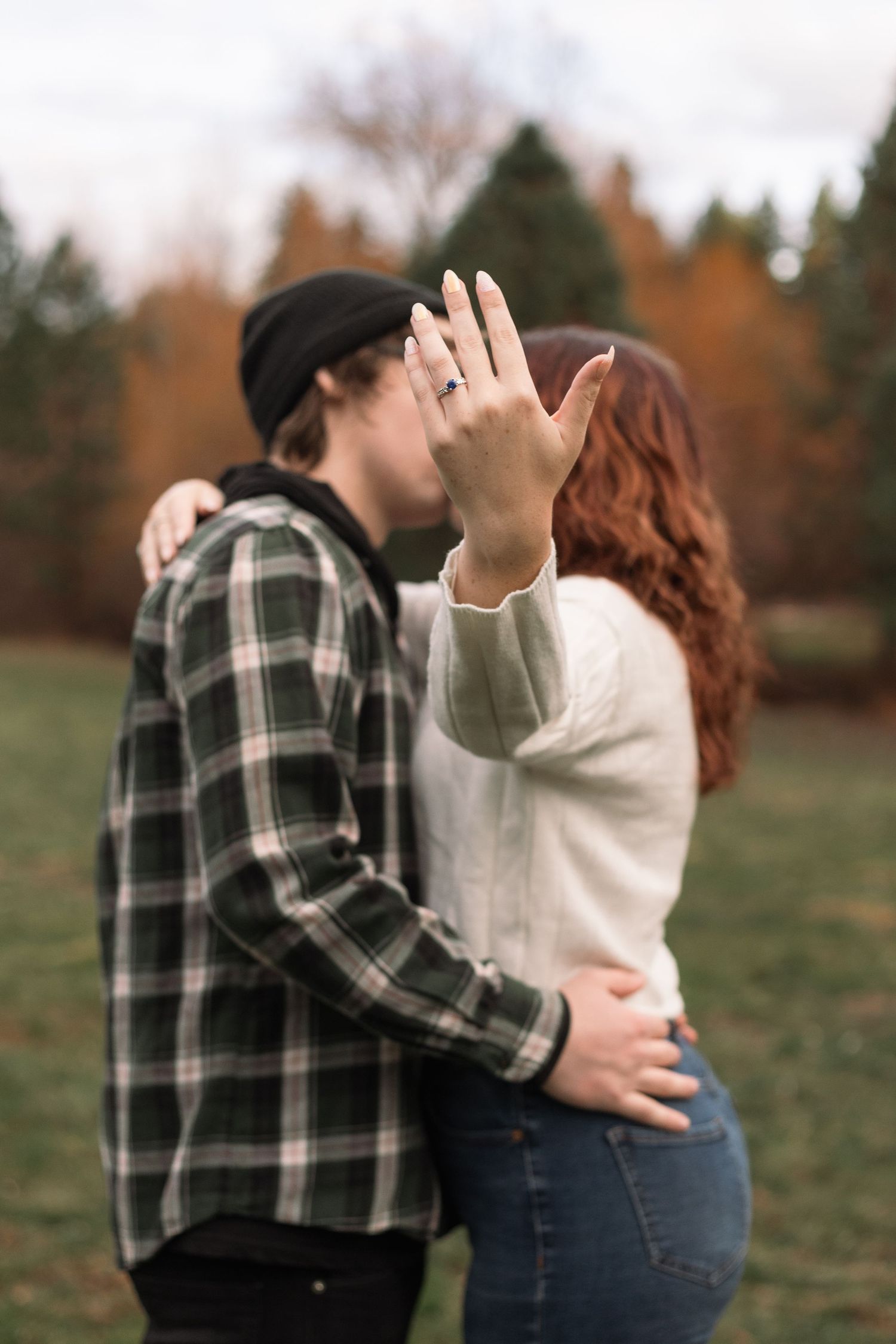 A couple embraces during an autumn photoshoot in a park with plaid and white outfits.