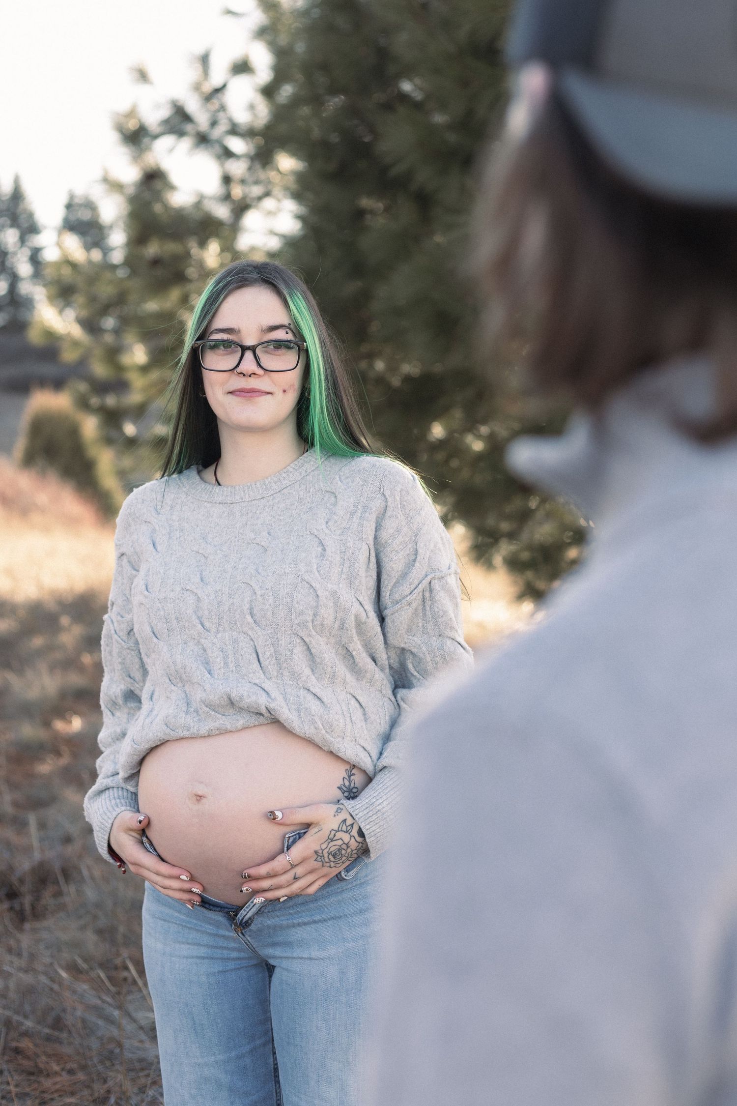 A maternity photoshoot featuring a cozy knit sweater and casual jeans in an outdoor setting.