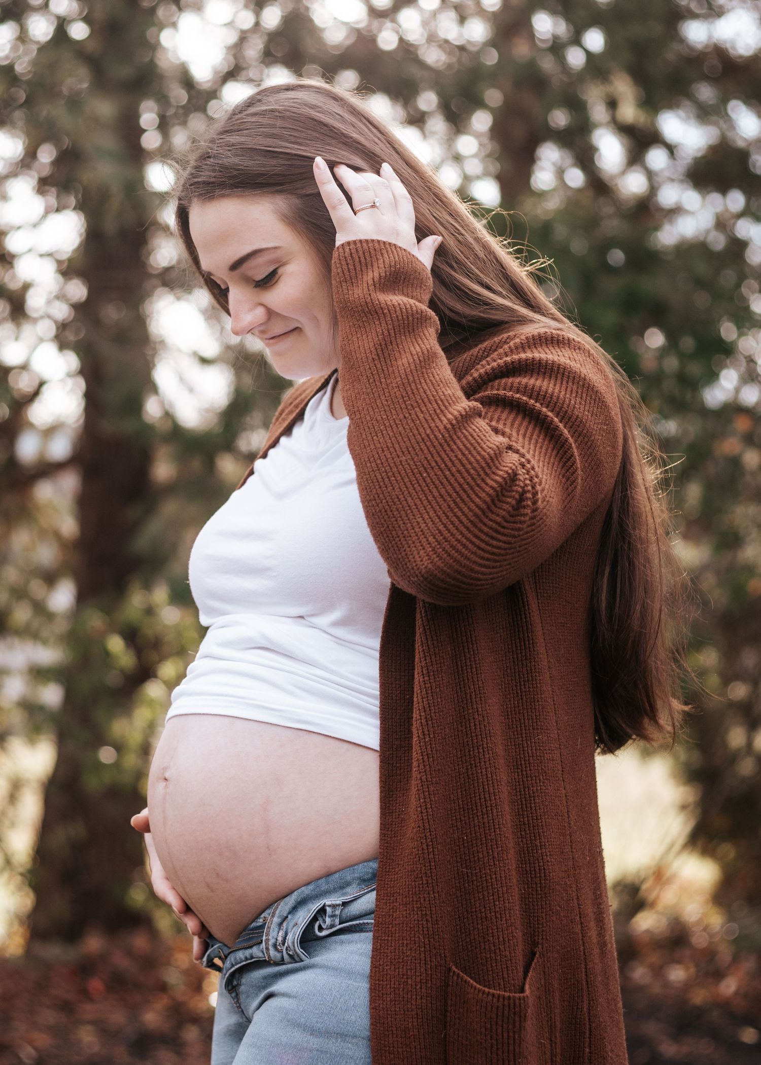 Maternity photo series showing woman in brown sweater and white top displaying growing baby bump outdoors.
