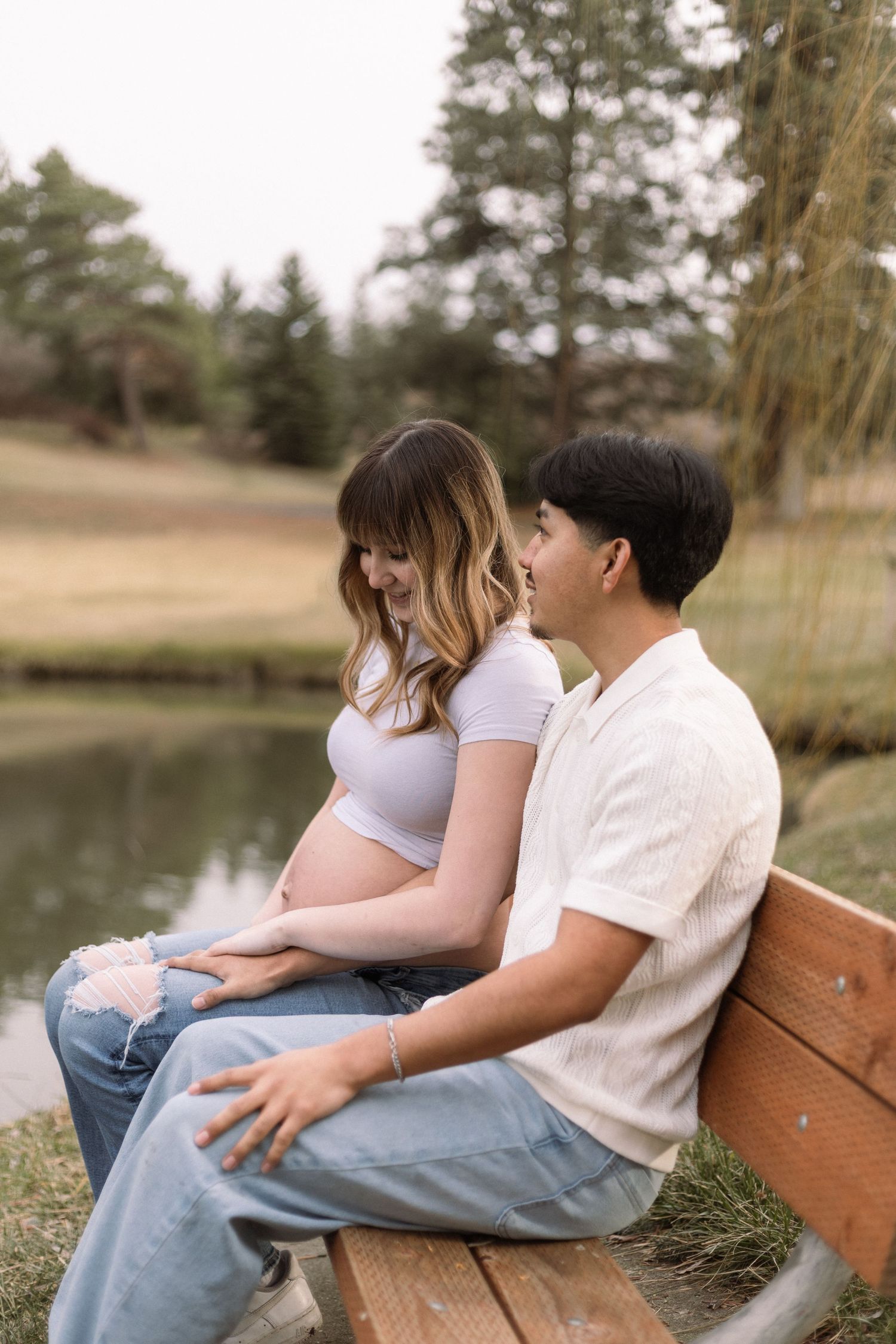 A couple sits together on a wooden bench near a serene lake during a peaceful outdoor moment.