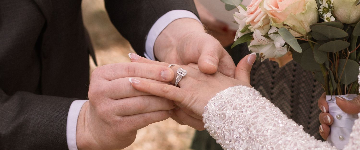 Close-up of hands exchanging wedding rings during an intimate ceremony with white floral decorations.