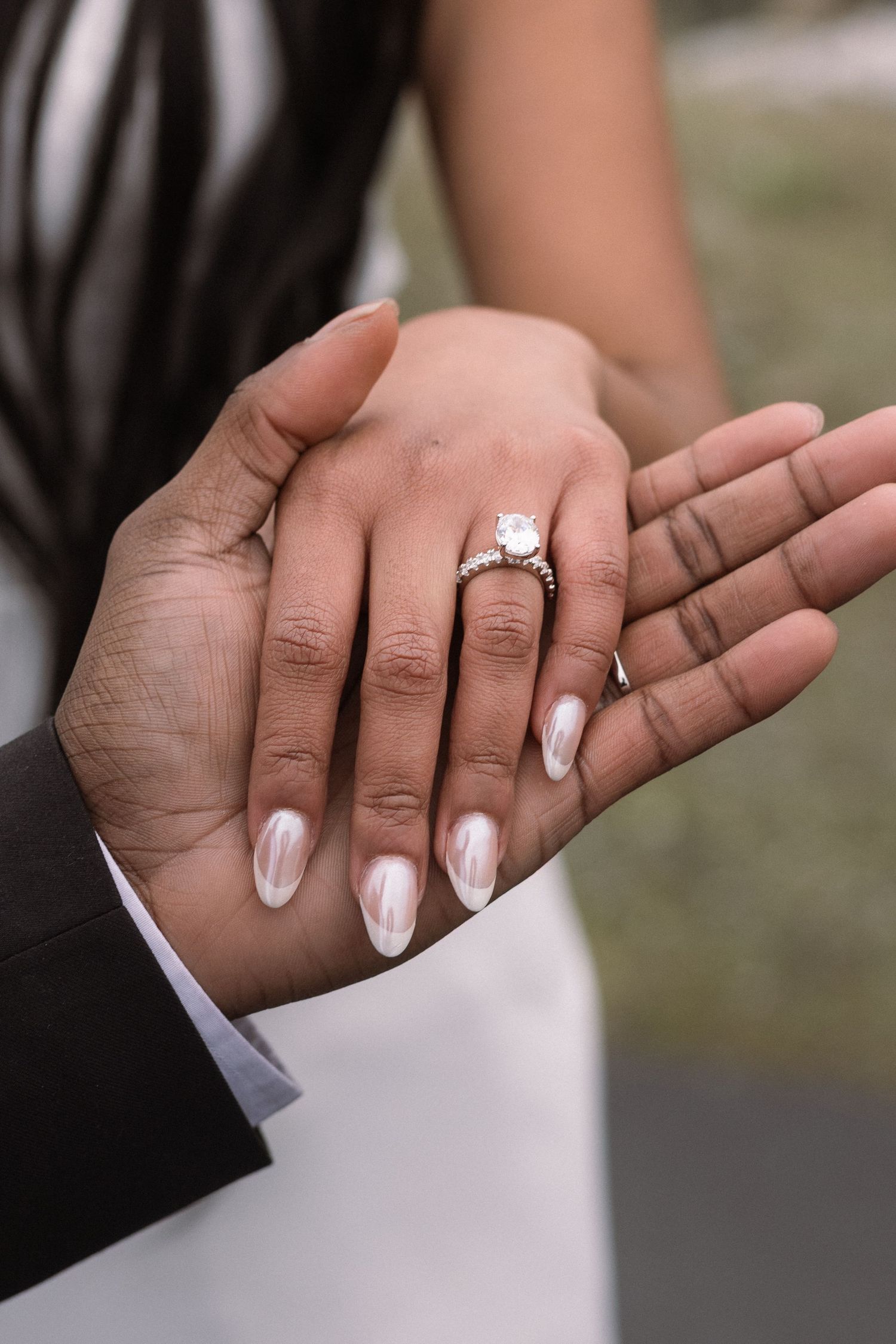 Close-up of hands showing engagement ring with white manicured nails.