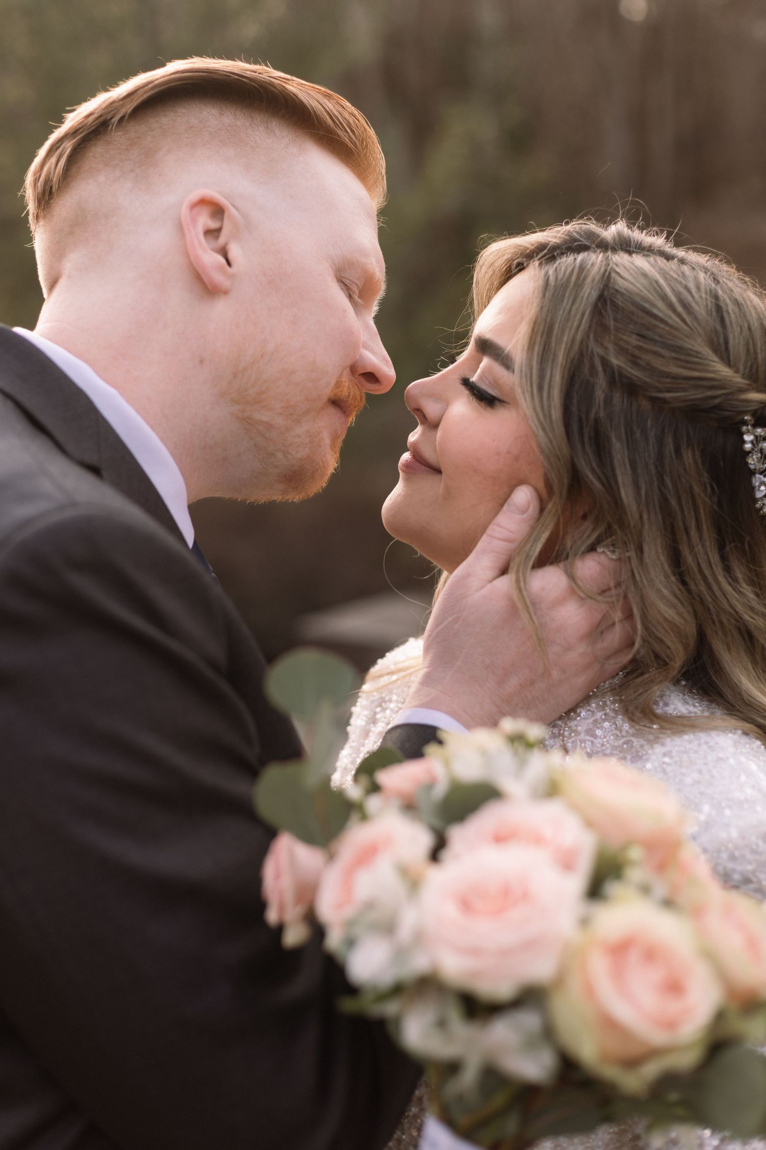 A romantic wedding moment captured between a couple with a soft pink rose bouquet in the foreground.