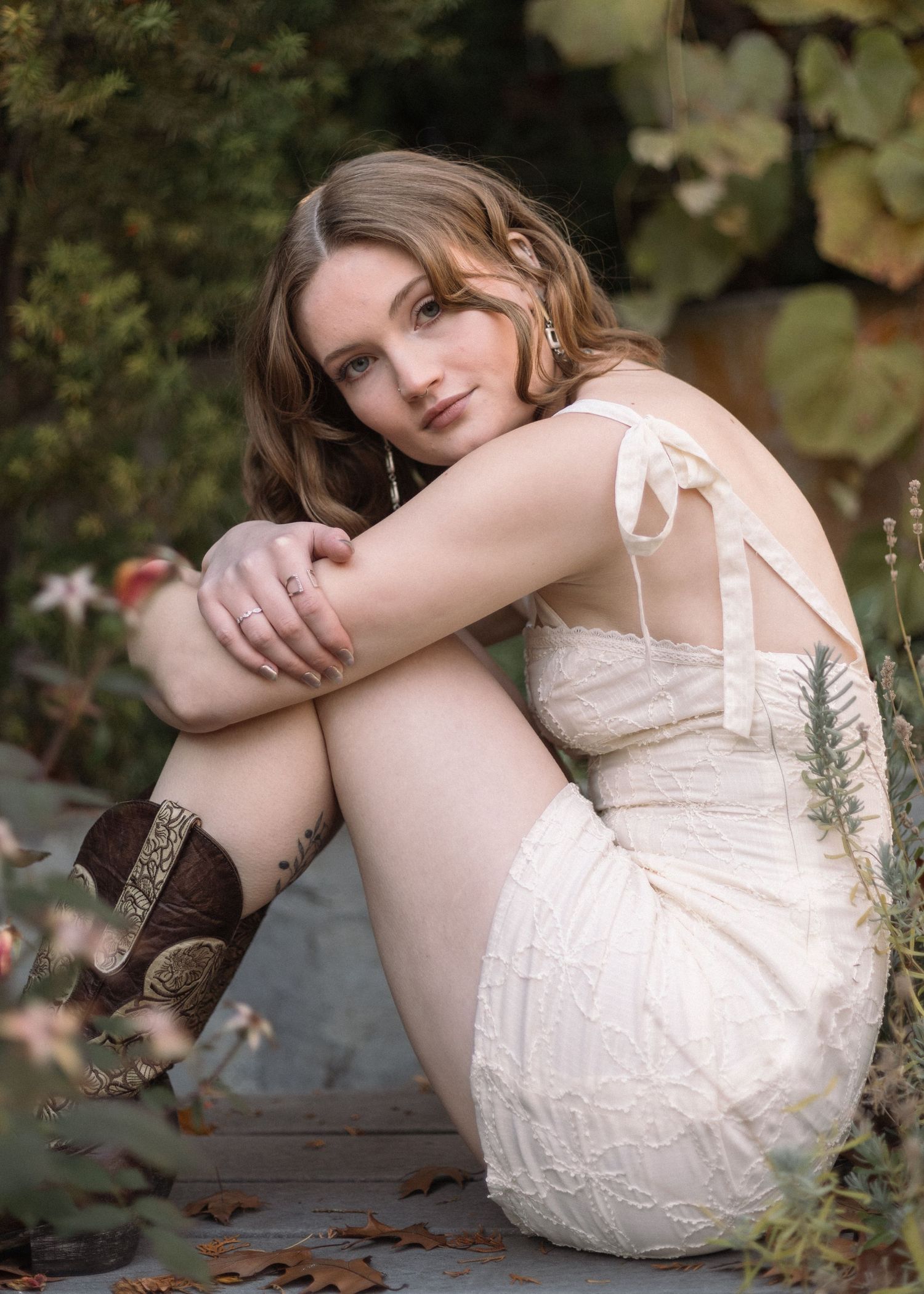 Artistic maternity photos in white lace dress among garden foliage.