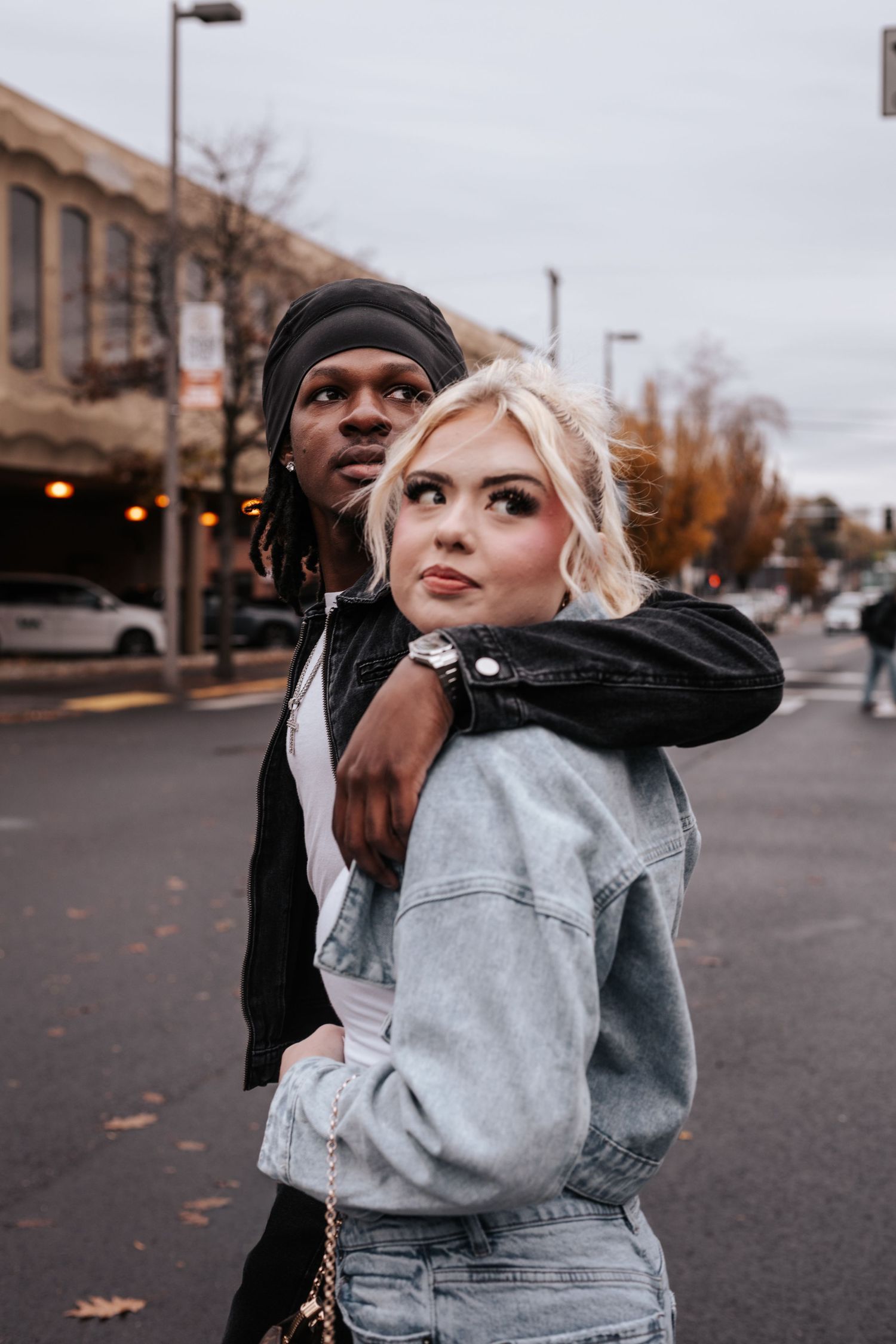 A couple in casual attire share an intimate dance moment on an urban street during autumn.