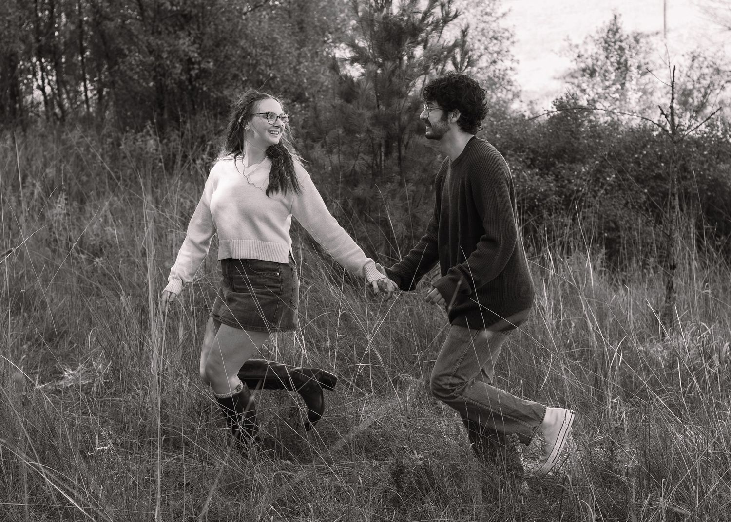 Artistic black and white photo of couple walking through tall grass.