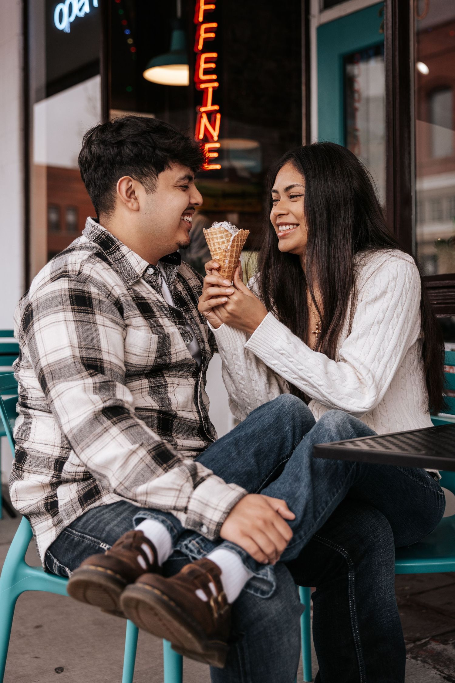 A couple shares ice cream cones while sitting together on a bench, laughing and enjoying a sweet moment.
