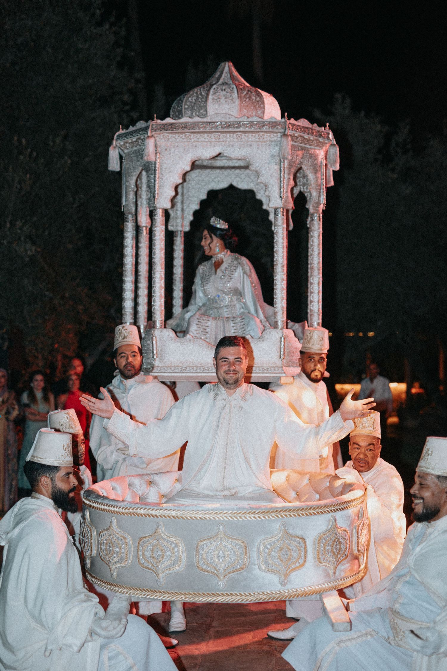 Bride and groom seated in a traditional Moroccan Amaria carried by four men during the wedding procession
