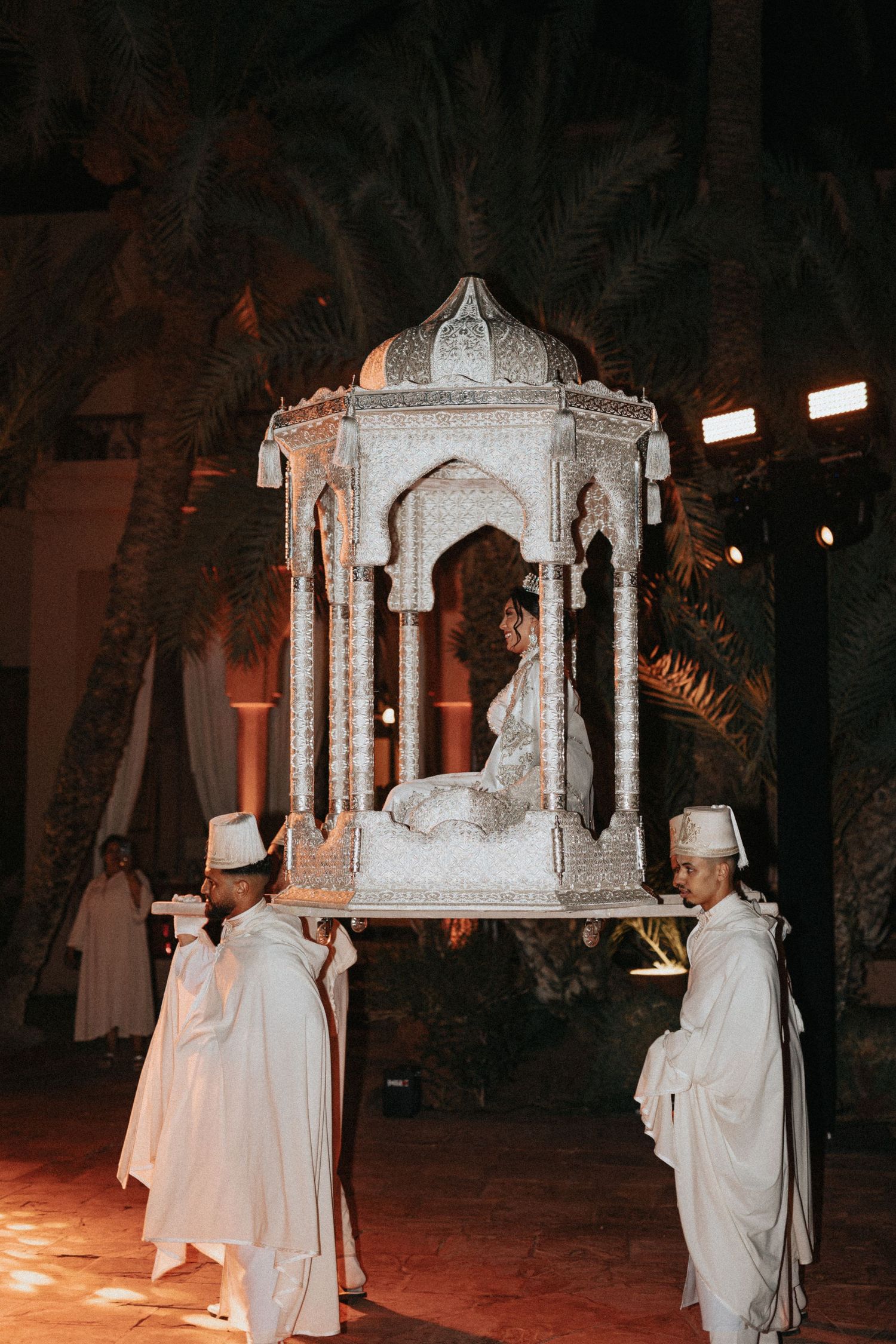 Bride seated in a traditional Moroccan Amaria carried by four men during the wedding procession