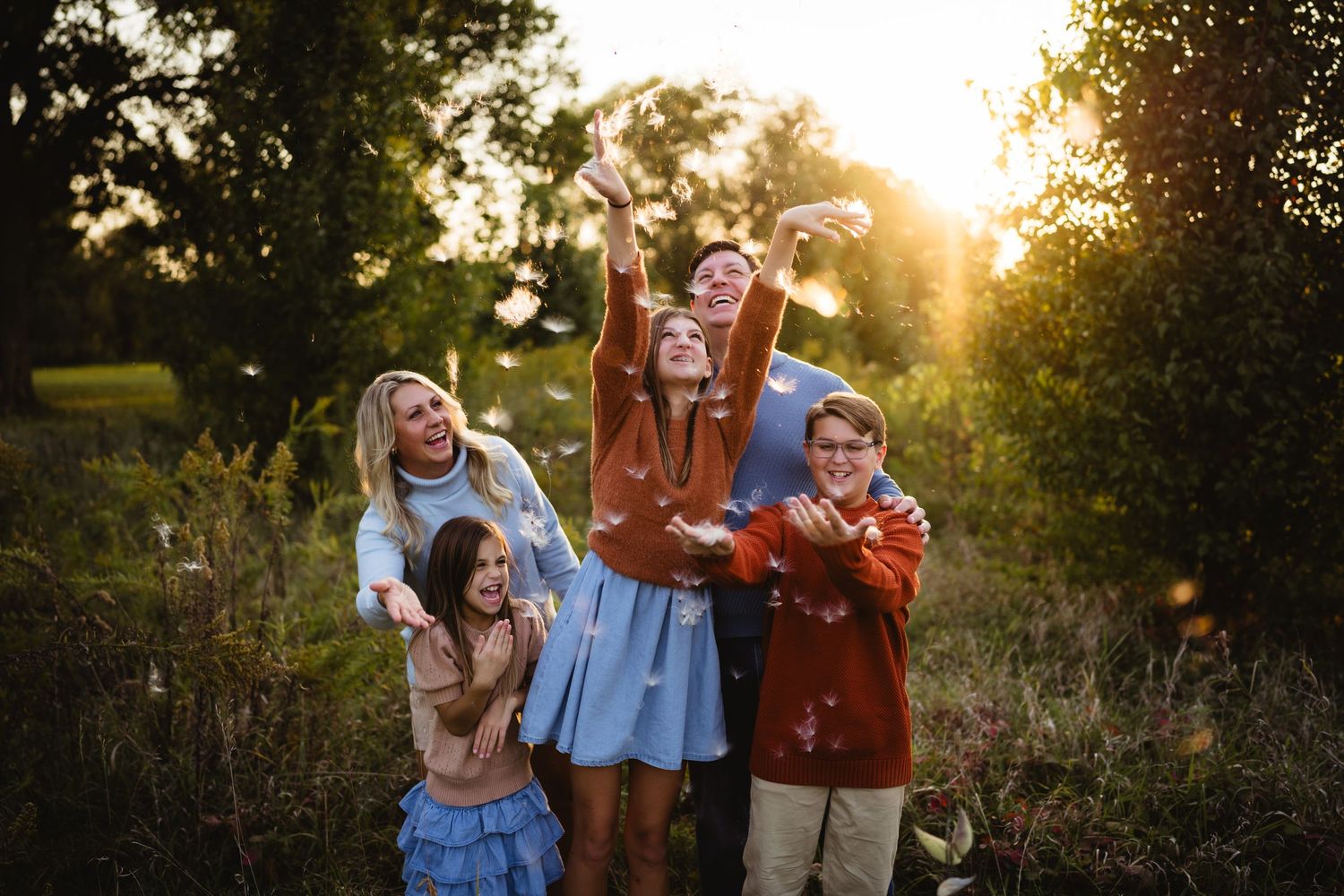 Family of five joyfully tossing confetti in a sunlit outdoor field during golden hour photography session.