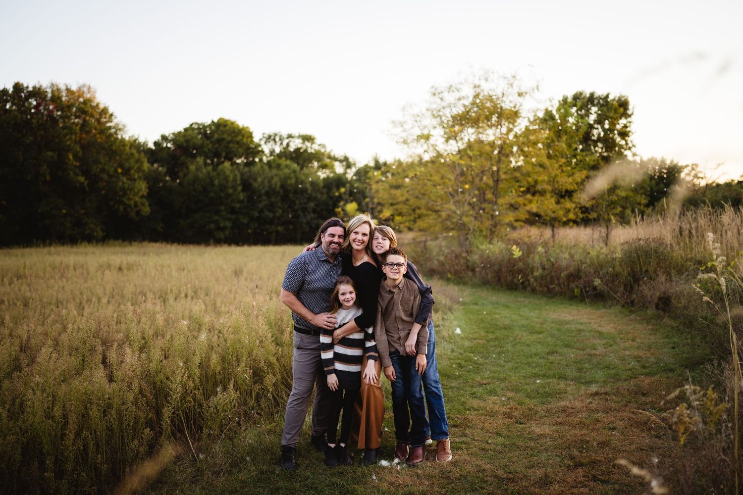 A family poses together in a beautiful autumn field during golden hour.
