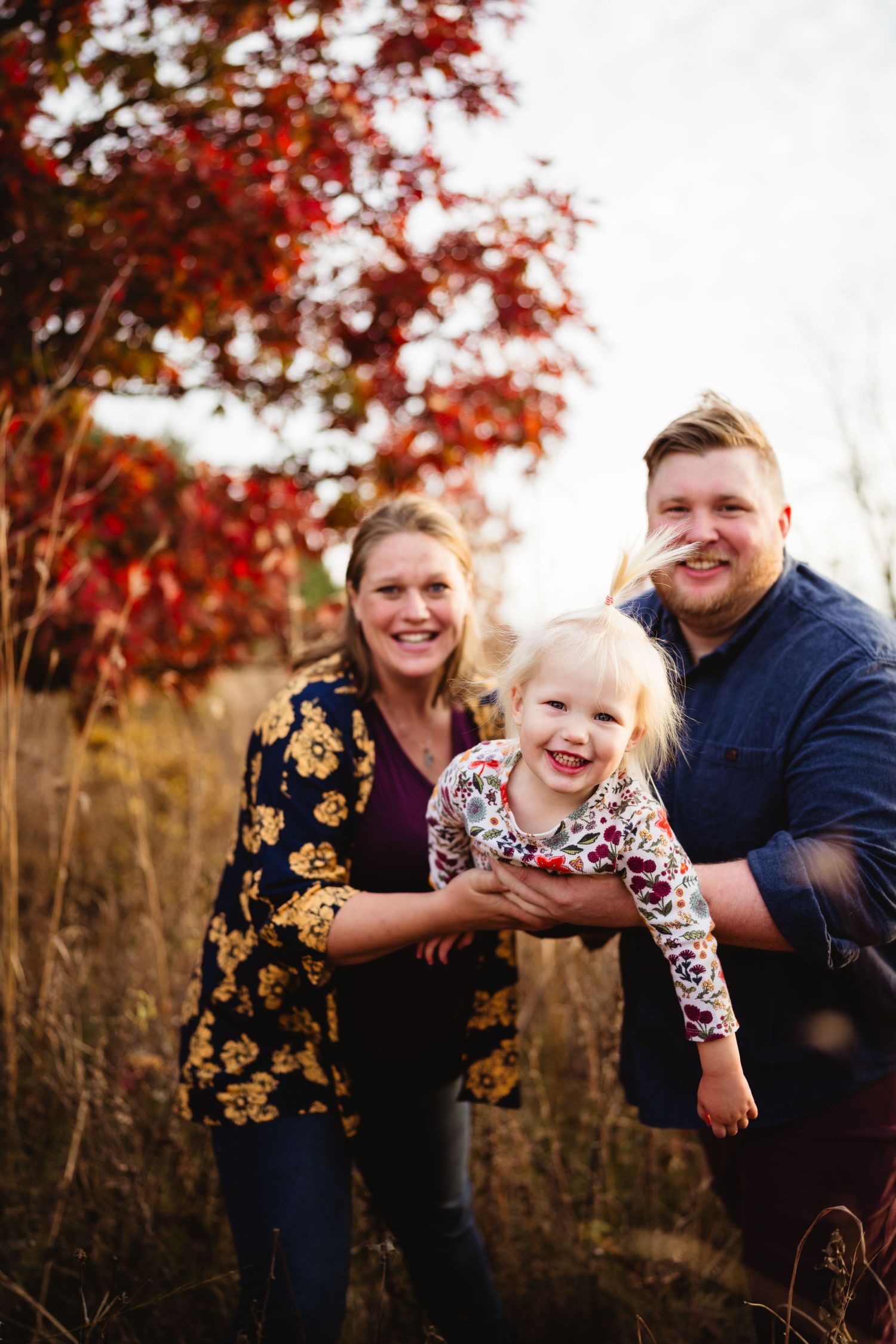 A joyful family moment captured in front of vibrant red autumn foliage.