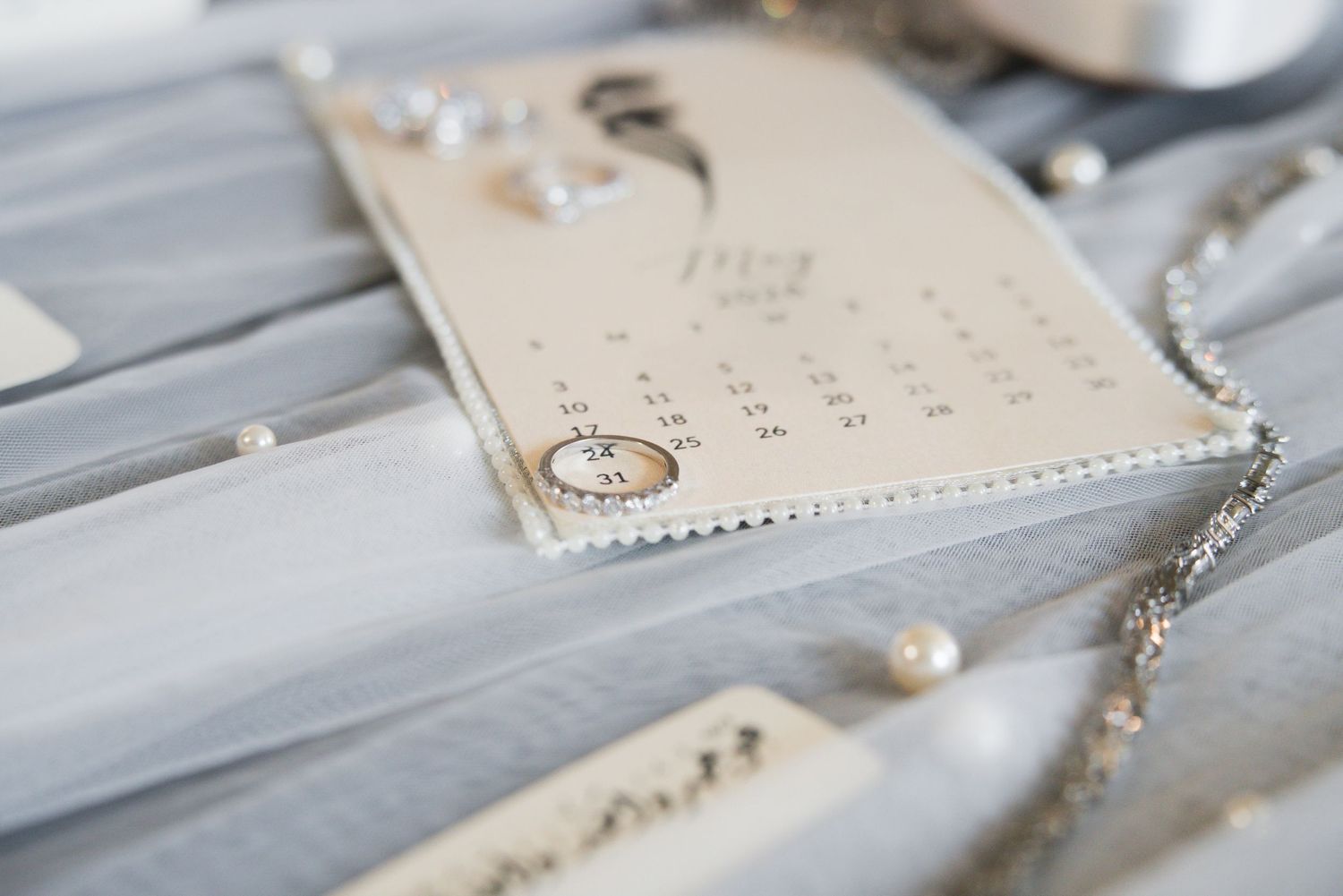 Wedding rings resting on a calendar with pearl jewelry and gray ribbon on a elegant flat lay display.