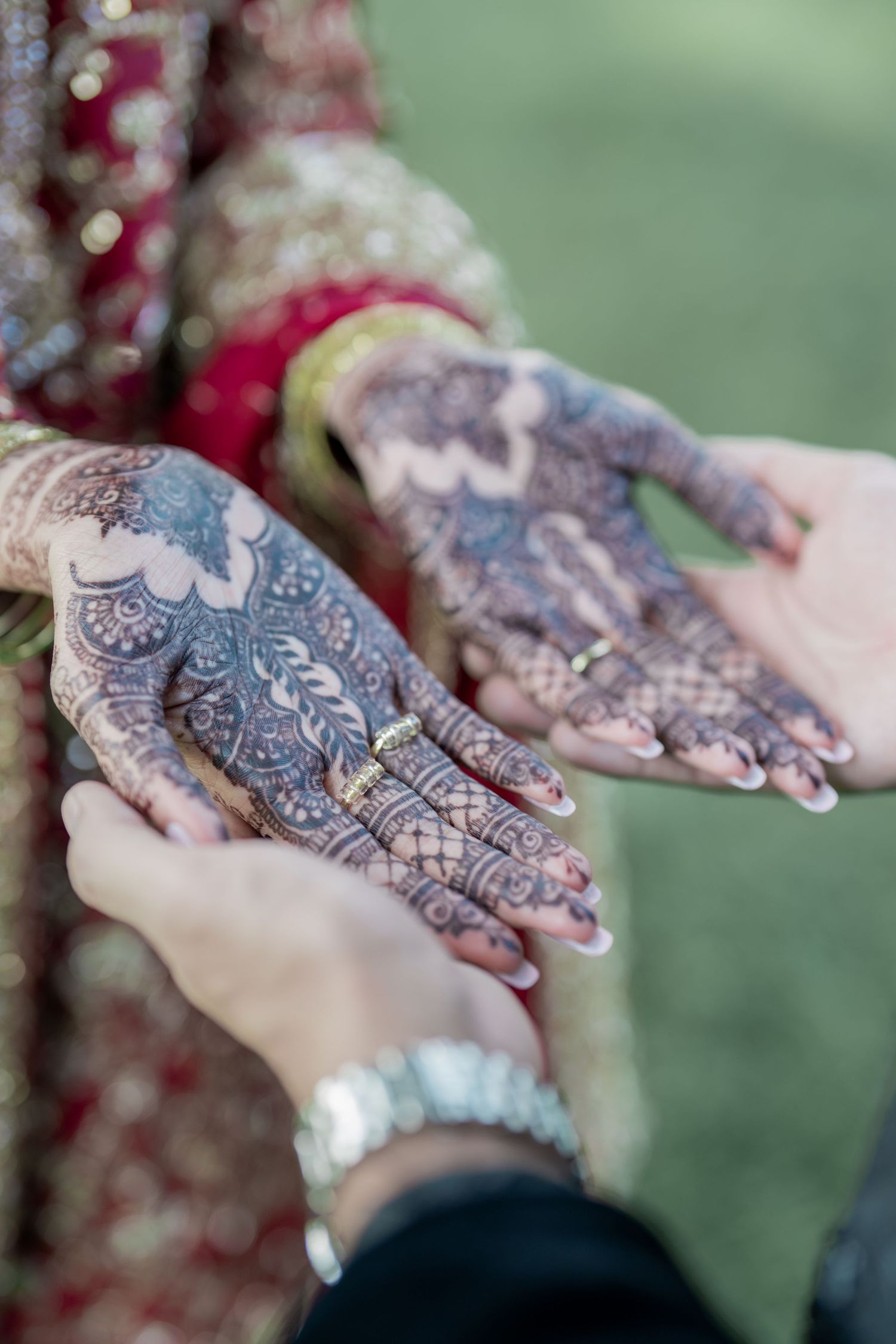 Bride displaying intricate henna mehndi designs on both hands, wearing traditional red bridal attire and gold rings.