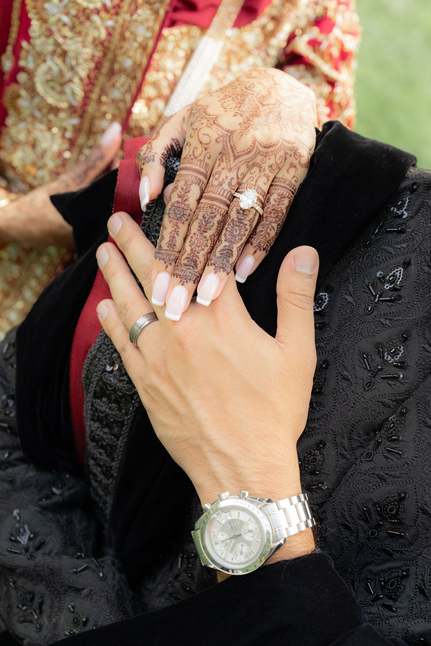 Bride with intricate henna mehndi design and diamond ring holds hands with groom wearing watch at South Asian wedding.