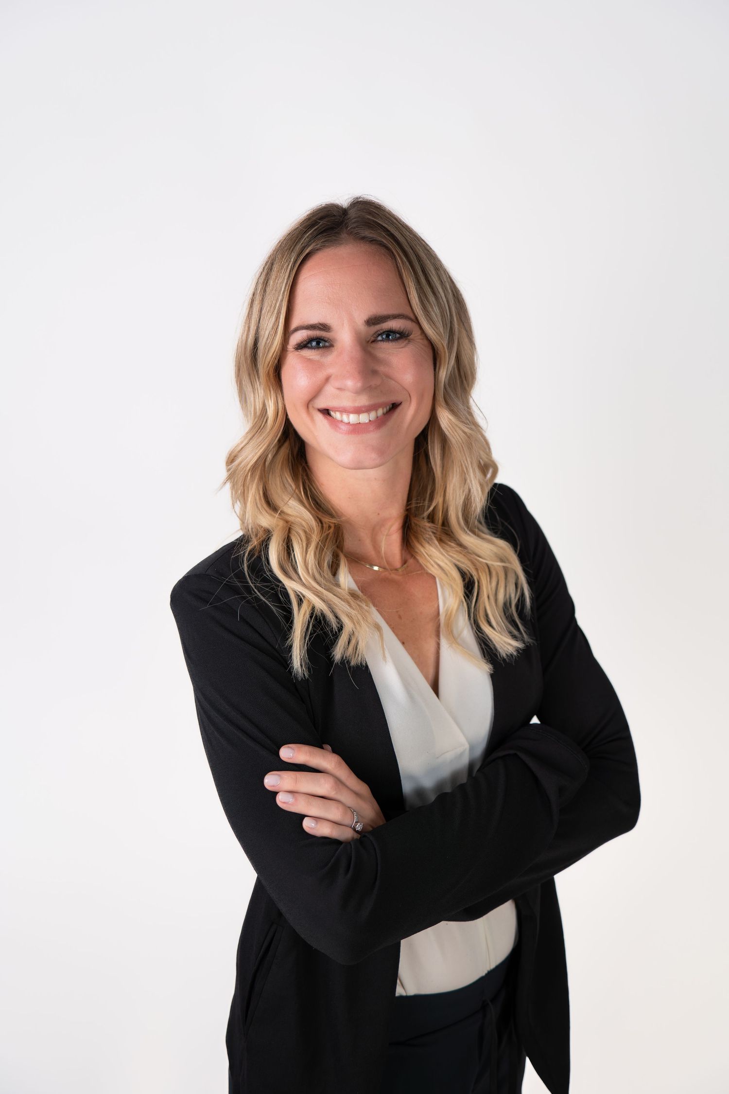 Professional in black blazer and white top poses against white studio background.