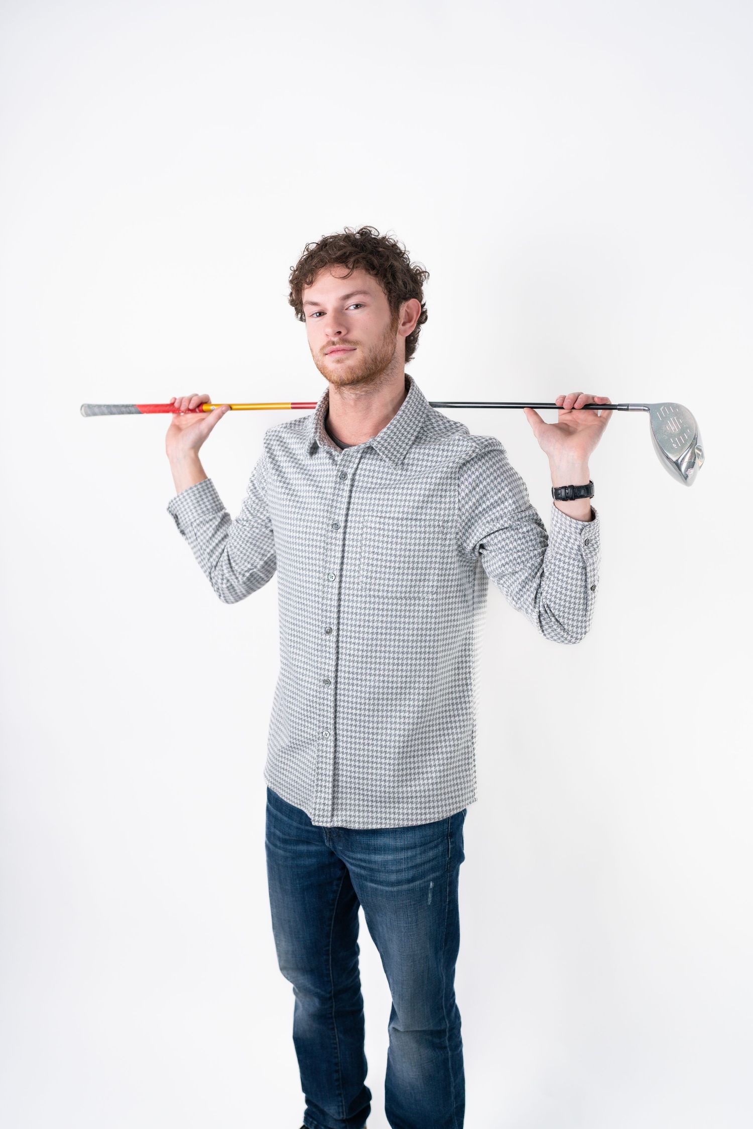 Person in checkered shirt playfully poses with golf club against white background.
