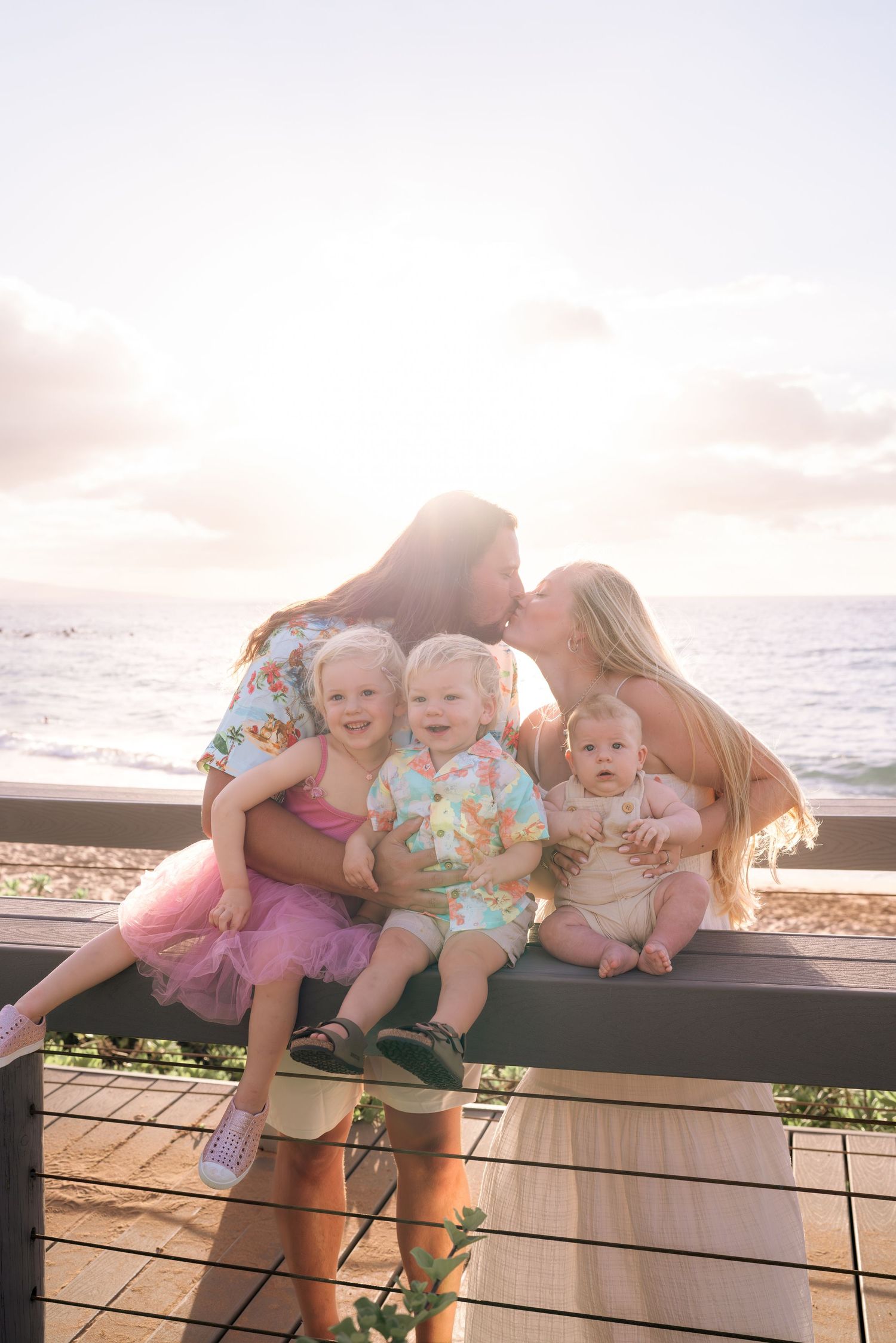 Family sharing tender moments on wooden deck overlooking ocean at sunset.