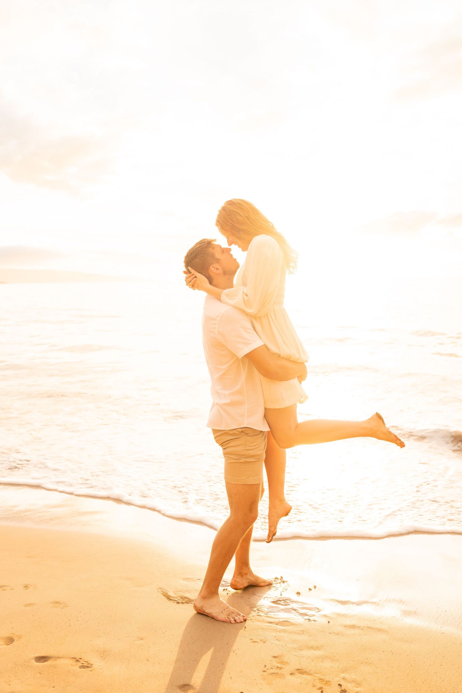 Silhouetted couple embracing on beach at golden hour with waves in background.