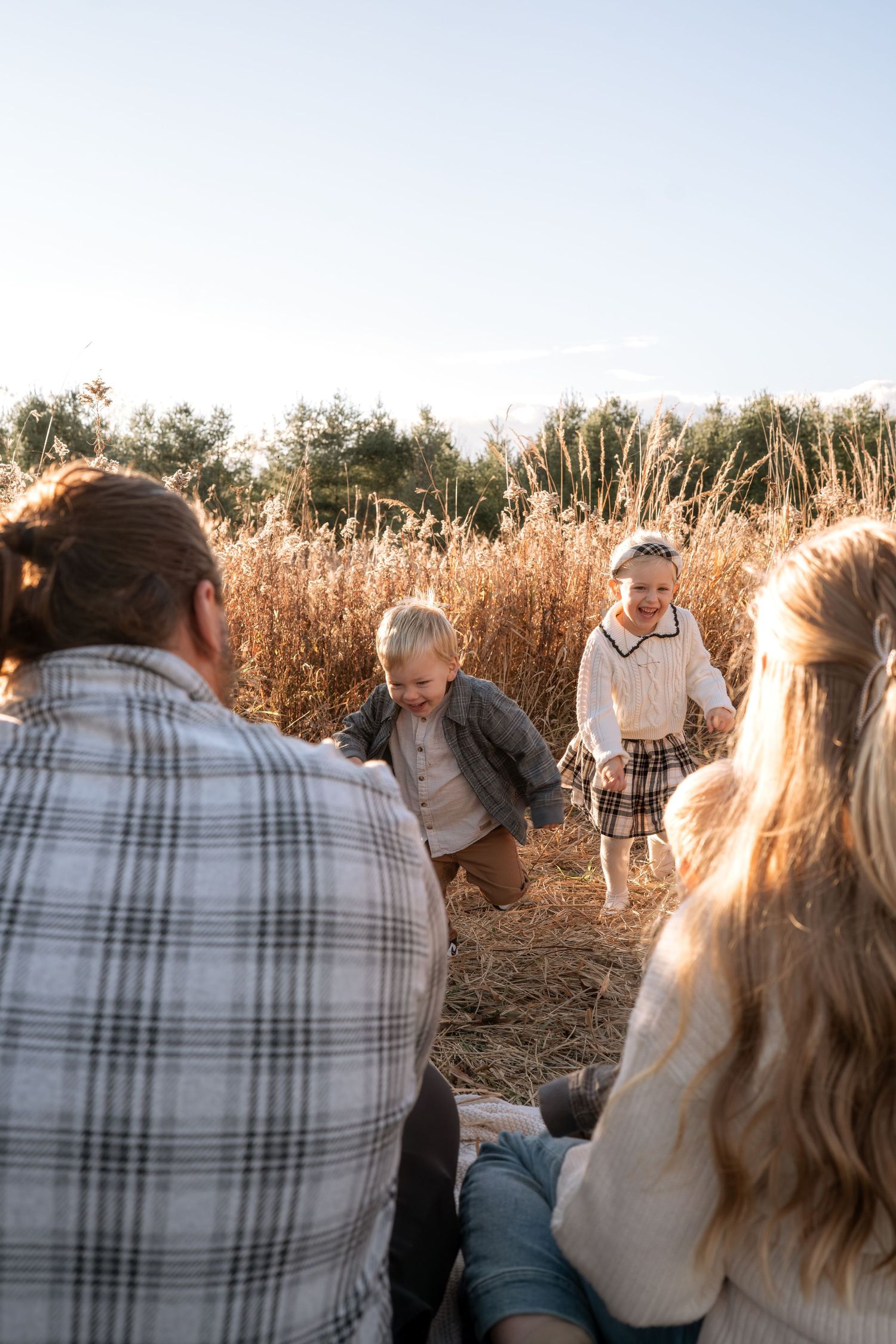 Family shares intimate moment on blanket in field at golden hour.