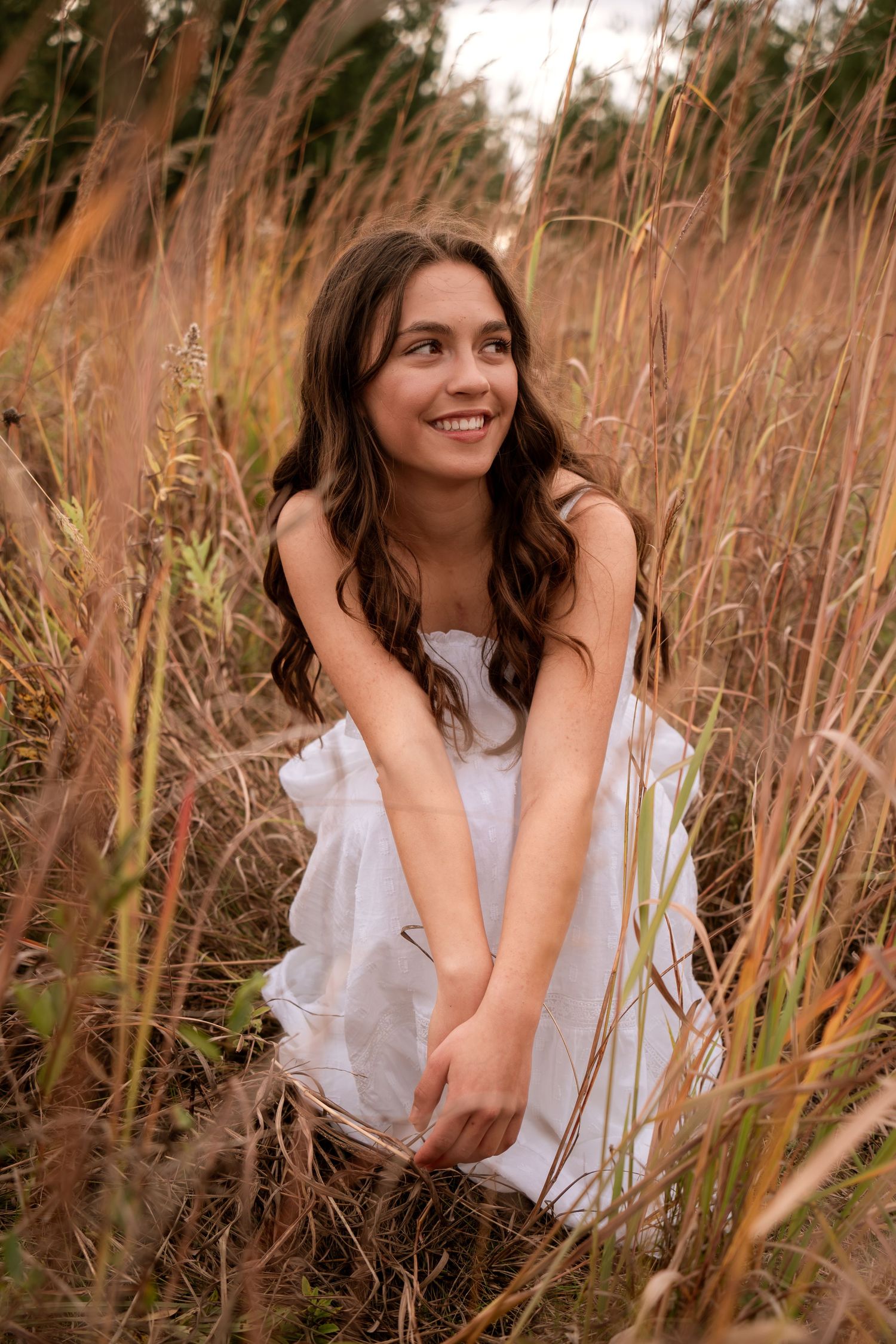 Person in white dress poses among tall golden grass during sunset.