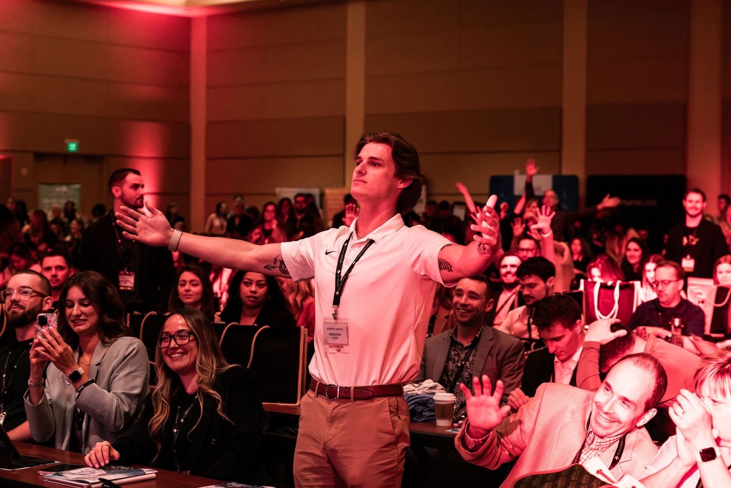 Audience members seated in rows with dramatic red lighting at a conference or event.