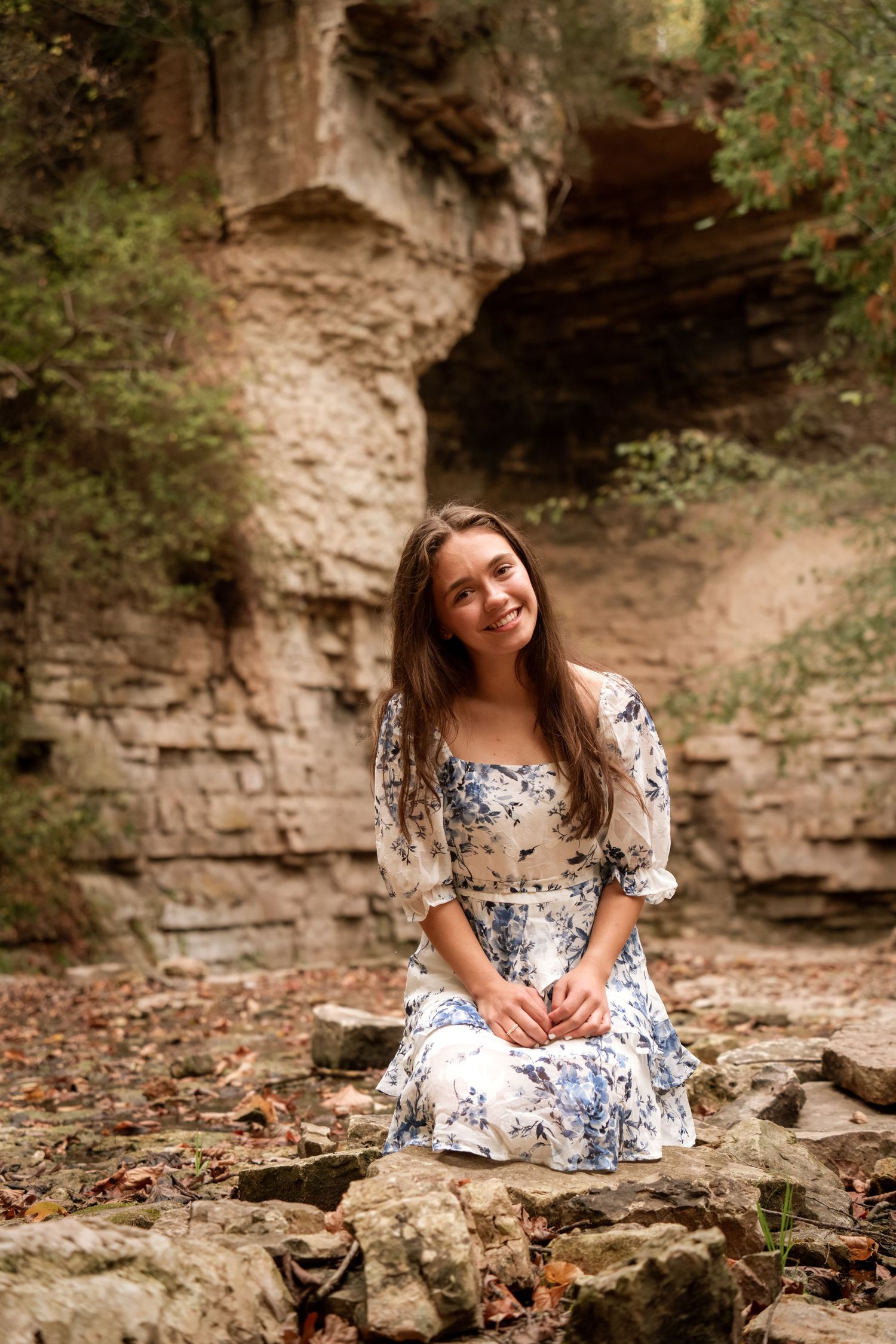 Person in floral dress poses on rocky terrain near limestone cliffs.