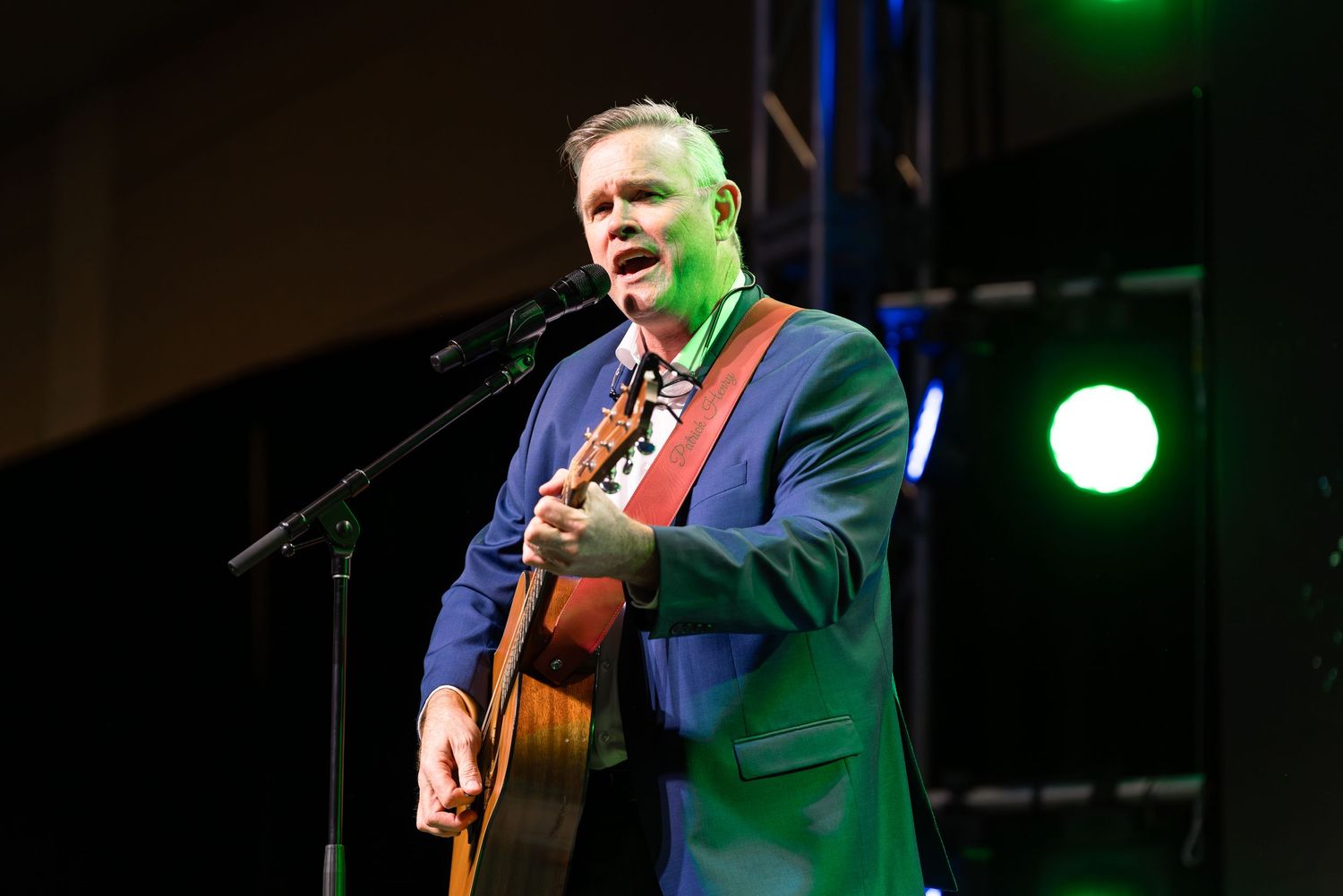 A performer plays acoustic guitar on stage with colorful lighting effects.