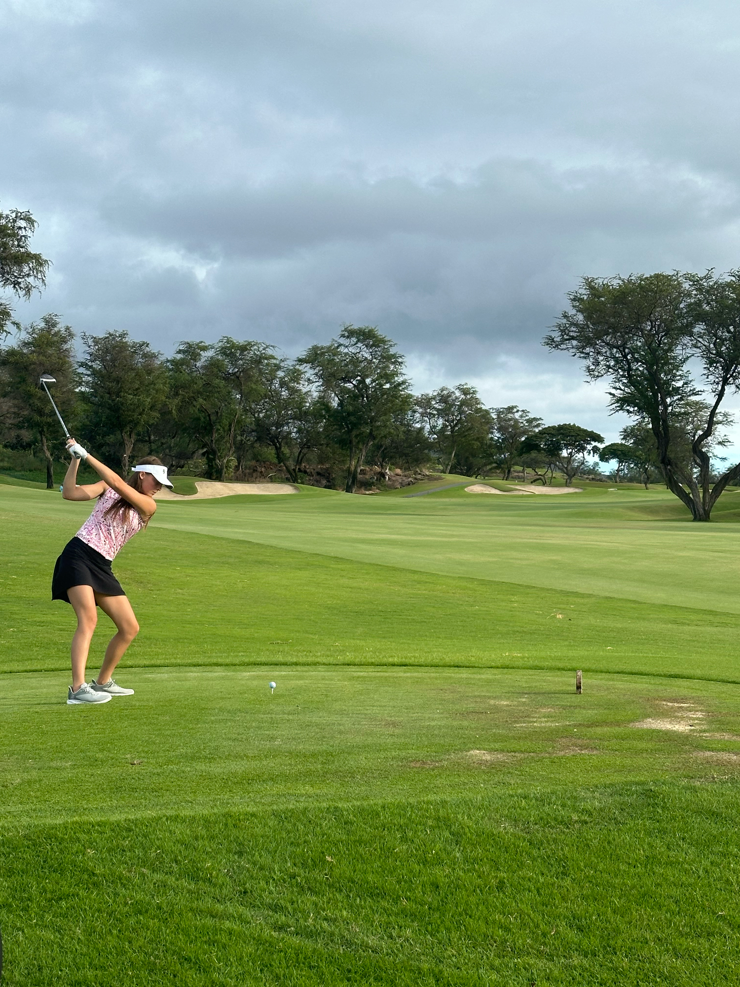 Golfer practicing their swing on a lush green course under cloudy skies.