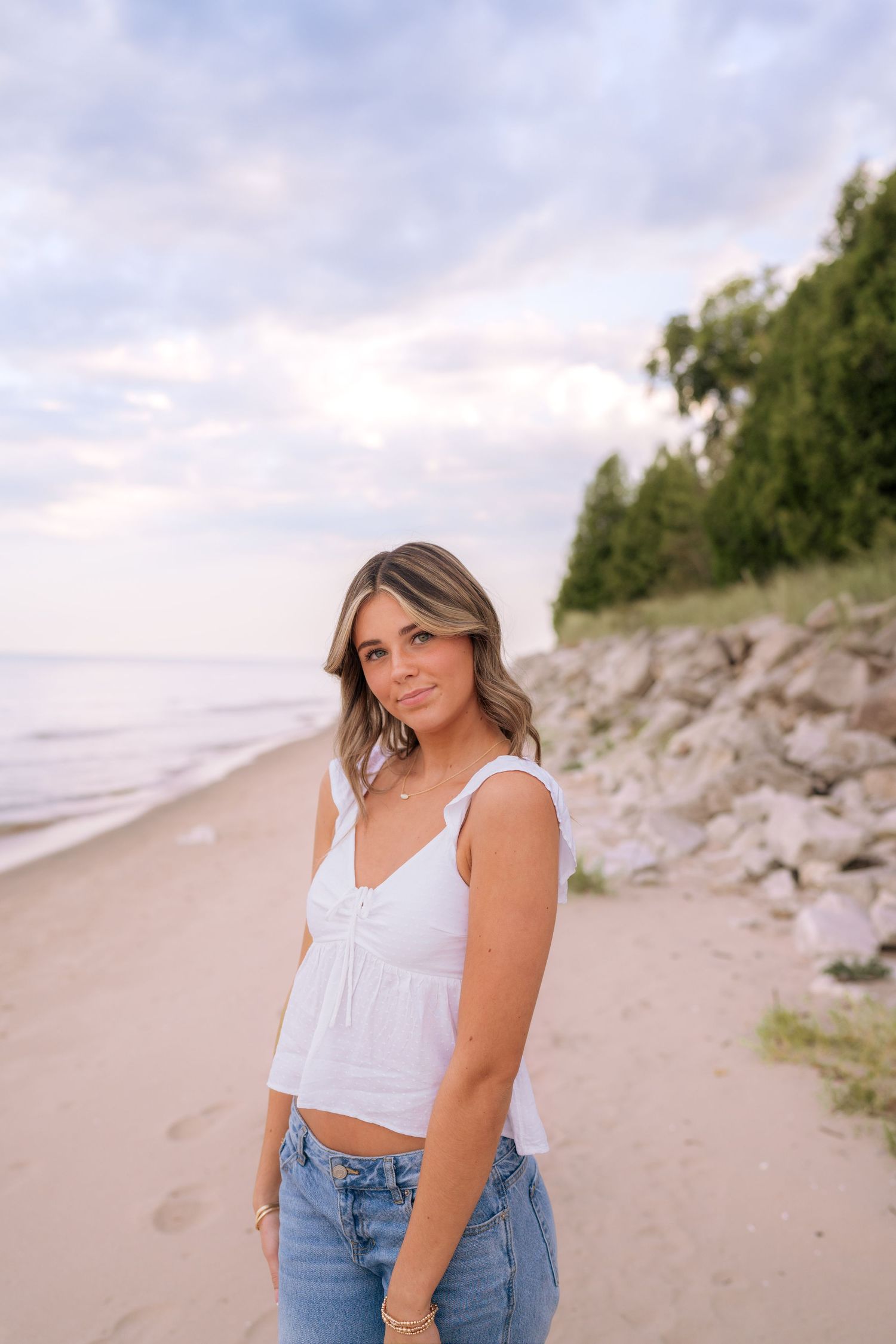 Beach photoshoot featuring someone in white top and jeans against sandy shore.