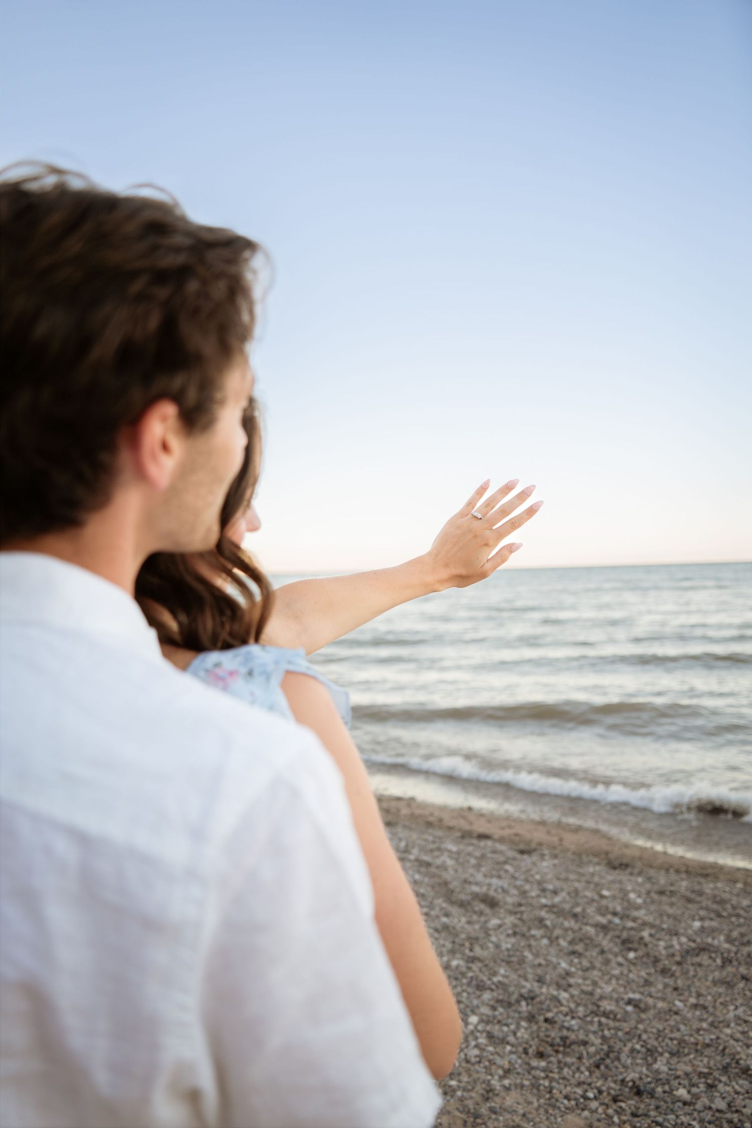 Couple in white clothing gesturing towards the ocean waves at sunset.