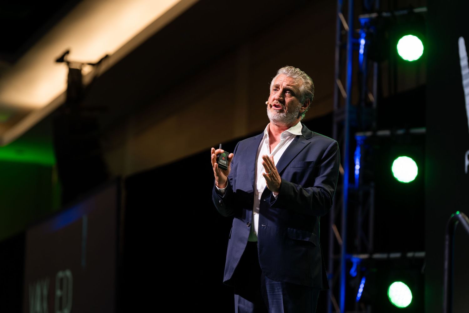 A speaker delivers an animated presentation under theatrical spotlights.