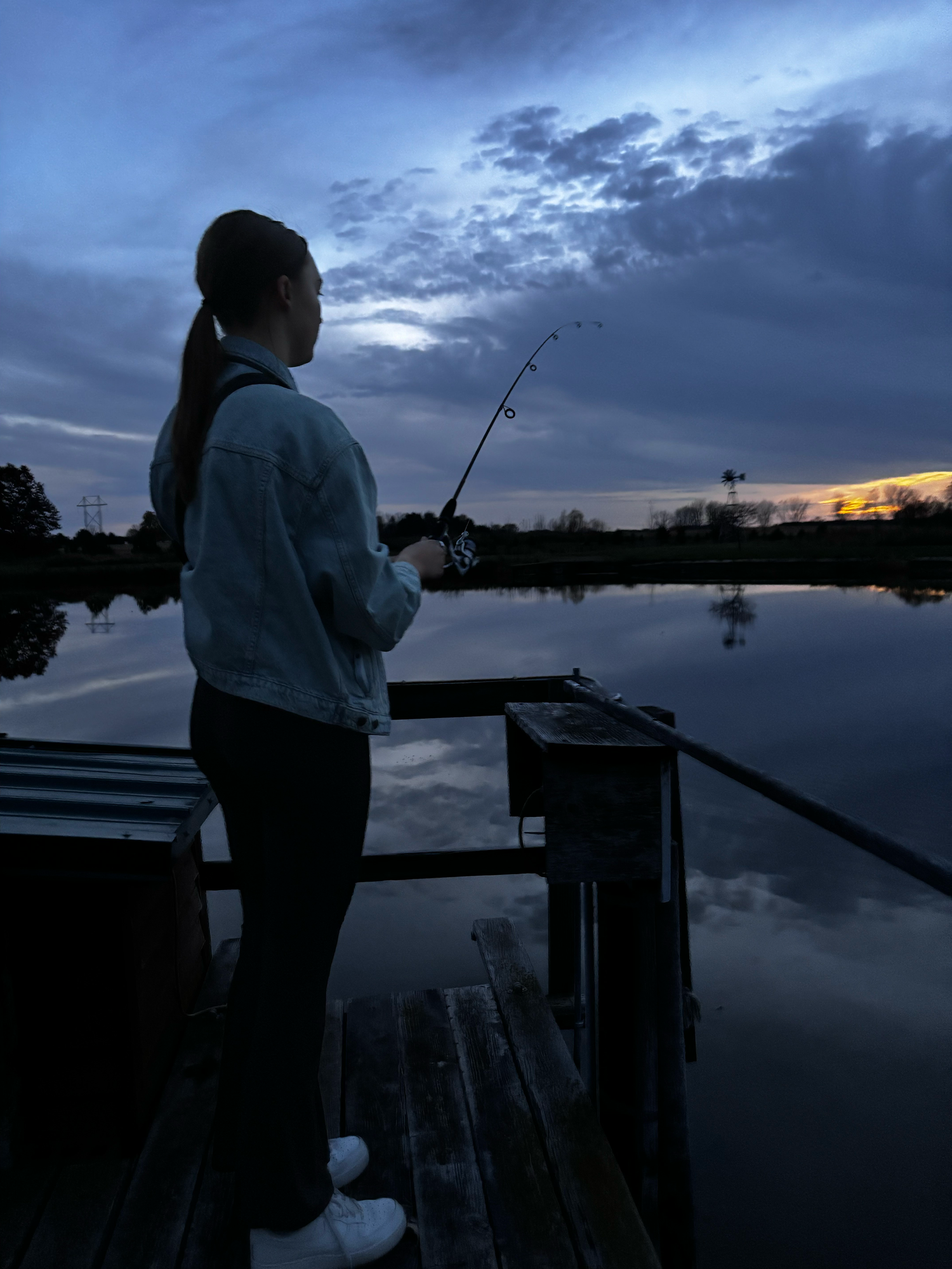 Silhouettes of people fishing at dusk against a dramatic cloudy sky.