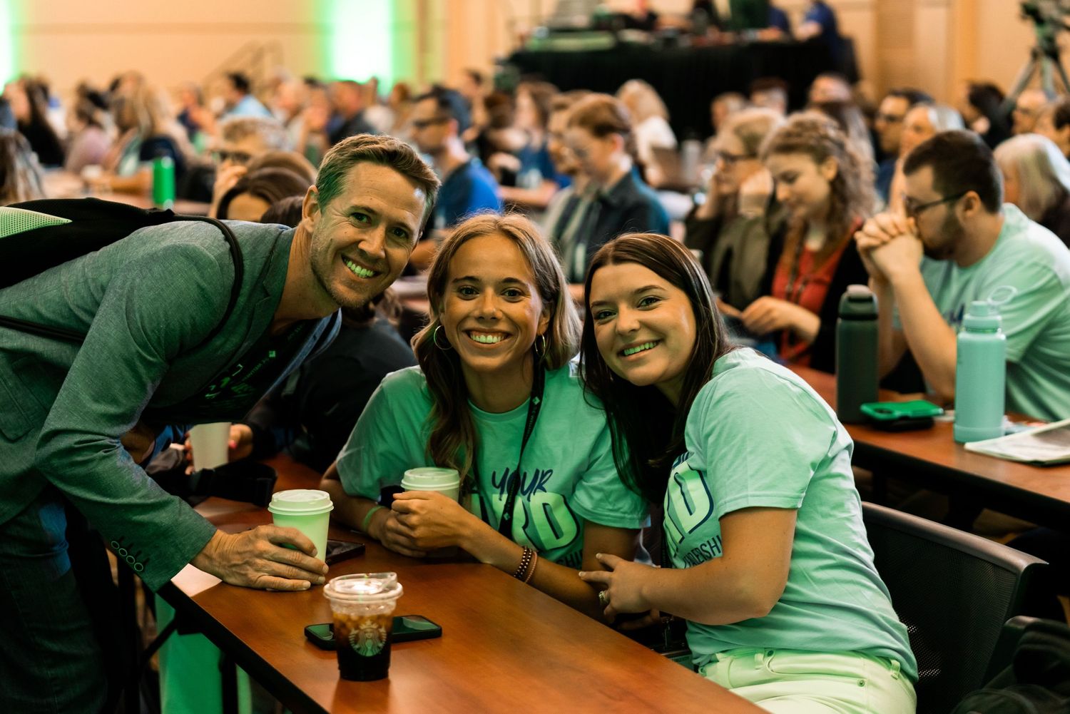 Conference attendees enjoying refreshments and conversation at tables with green ambient lighting.