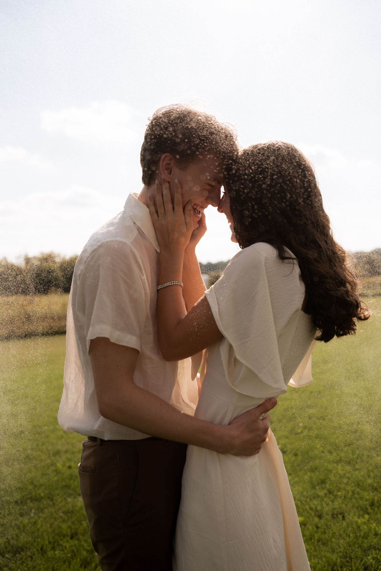 Romantic couple in white and casual attire embracing in sunlit field.