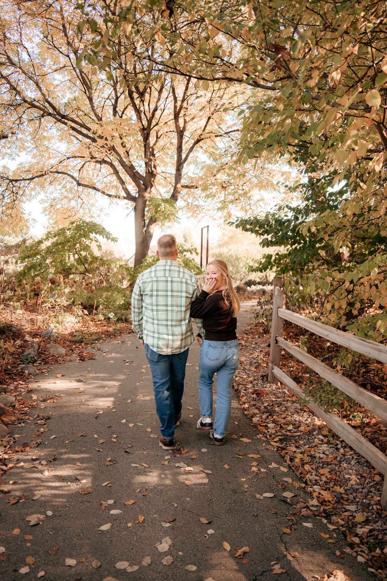 Couple walking together on a leaf-covered path through autumn trees.
