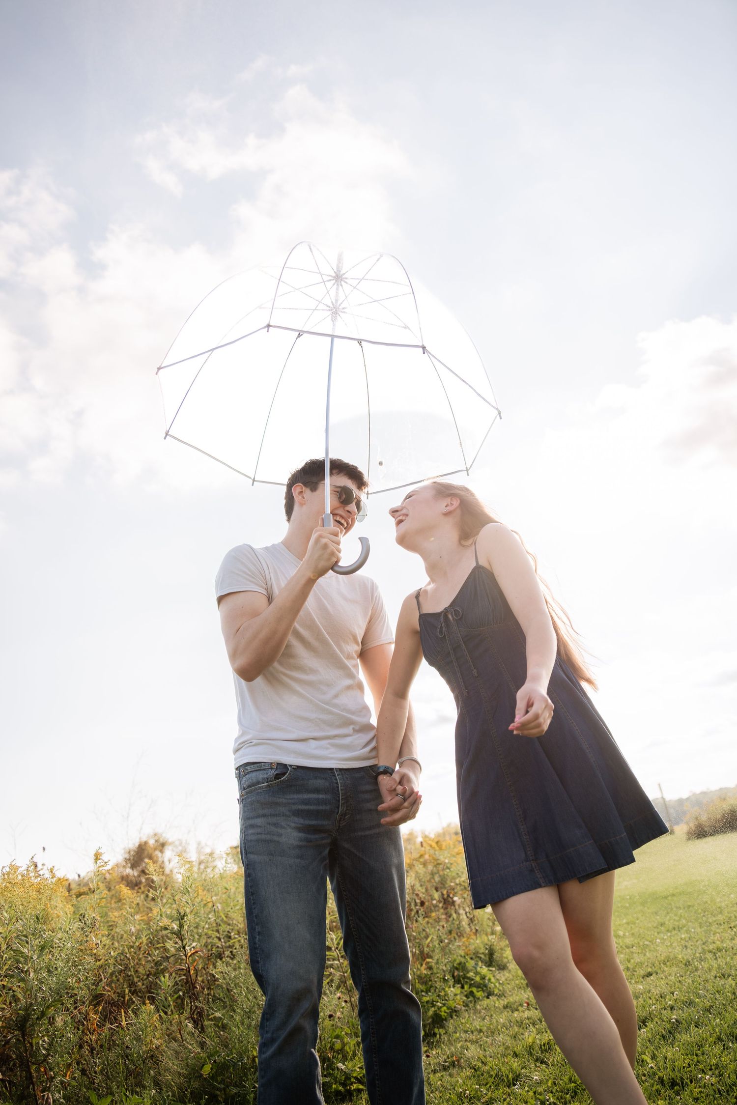 Playful couple poses with umbrella in summer field during sunset.