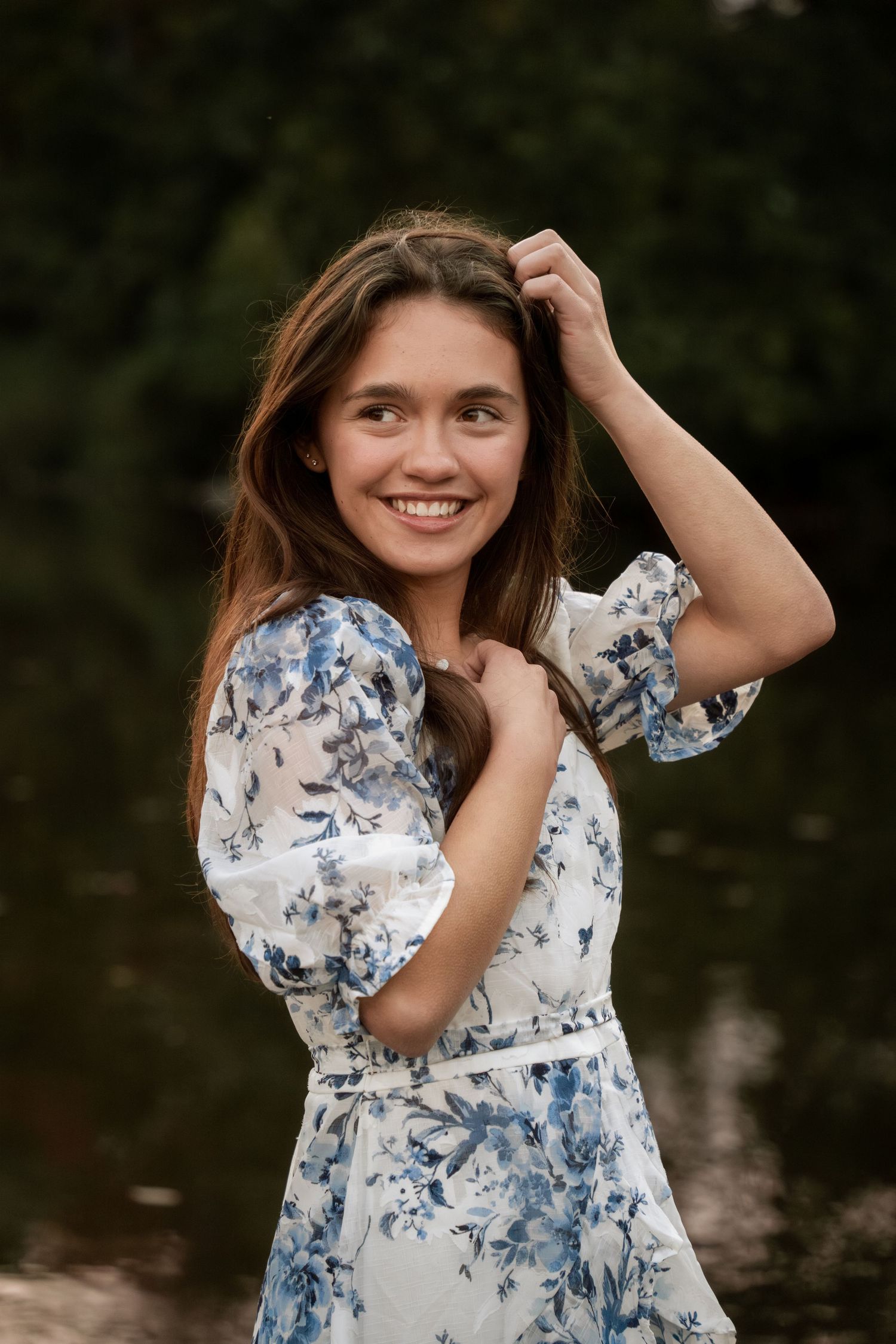 Person in blue floral dress poses outdoors with natural lighting.