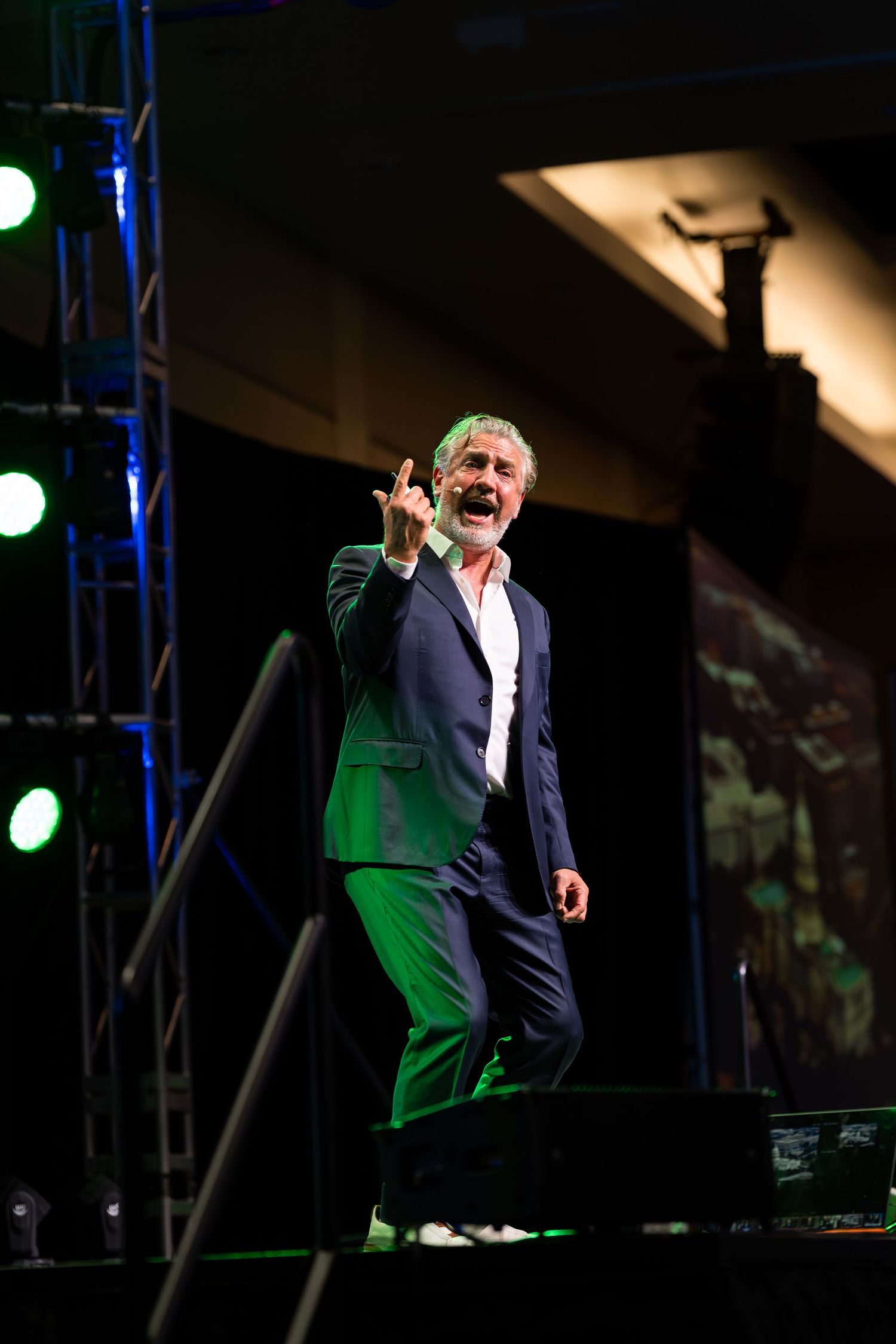 Animated speaker gestures expressively on darkened stage with green accent lighting.